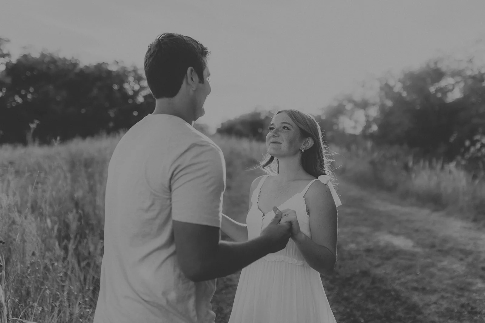 A couple holding hands and looking at each other in a field, smiling during sunset during their engagement photography session at Rock Bridge State Park in Columbia, MO.