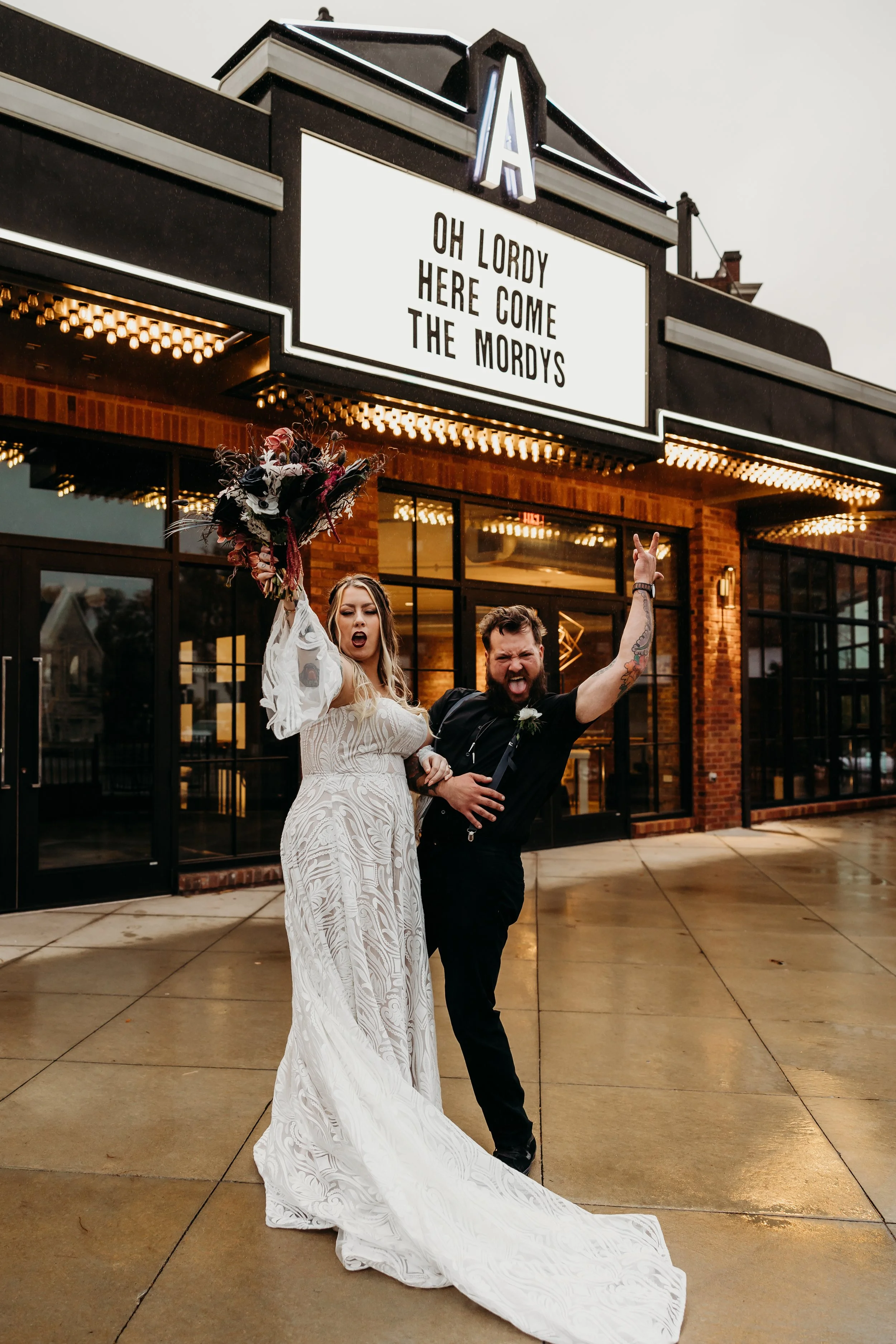 A gold wedding ring with gemstones resting on a textured white surface, surrounded by pale pink and cream flowers.