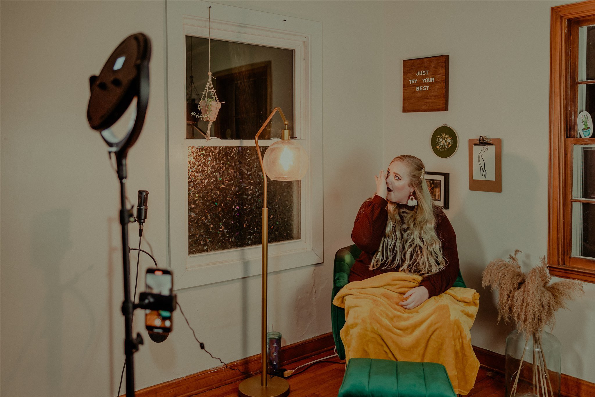 A woman sitting on a green chair with a yellow blanket on her lap in a cozy living room, looking surprised or engaged, during a trauma informed photography session in Columbia, Missouri.
