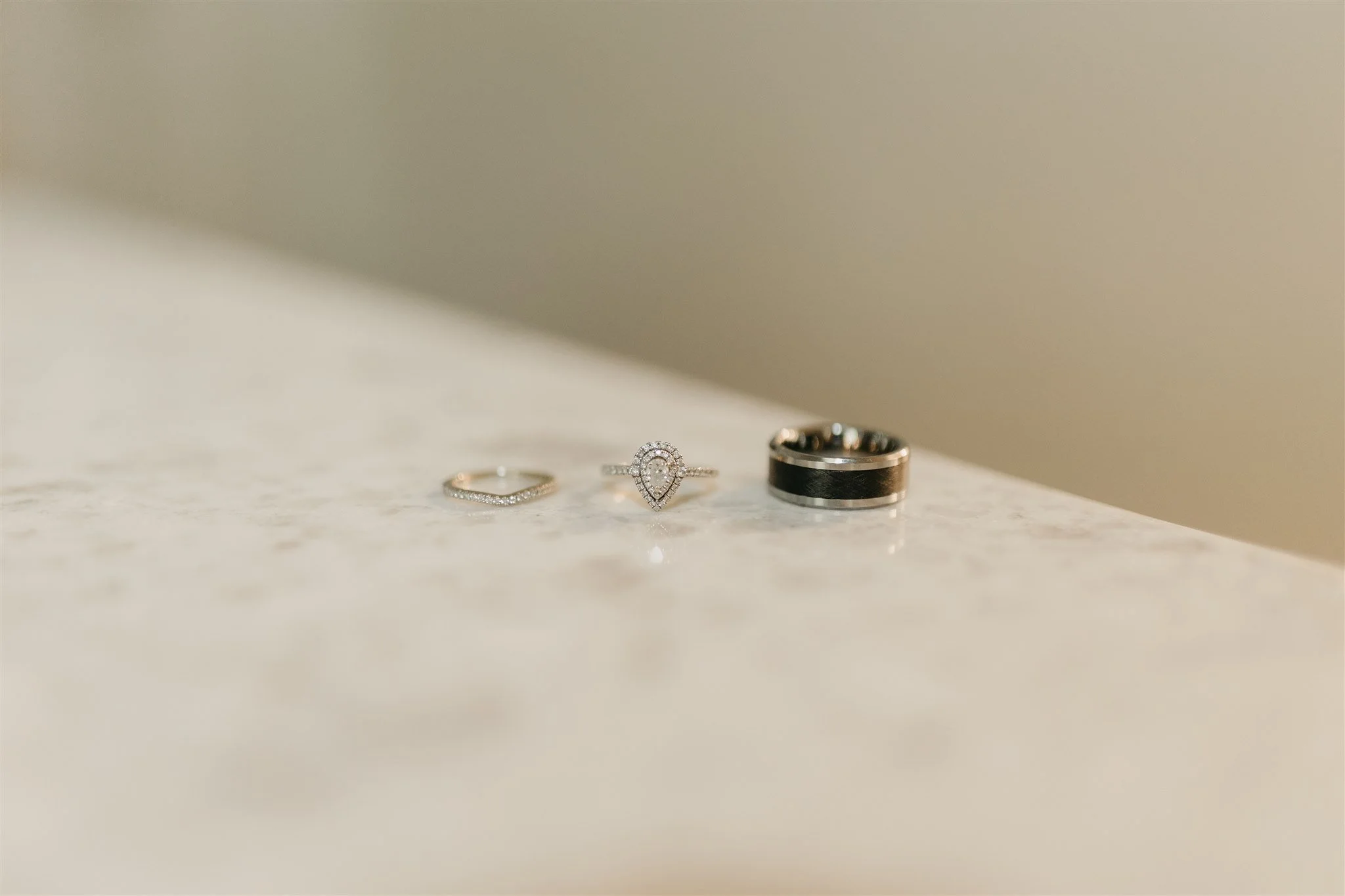 Three rings on a beige marble surface with a blurred background at Rolla, Missouri rustic wedding venue, The Village. Photos by Columbia, MO Photographer Liv Strange Photography.