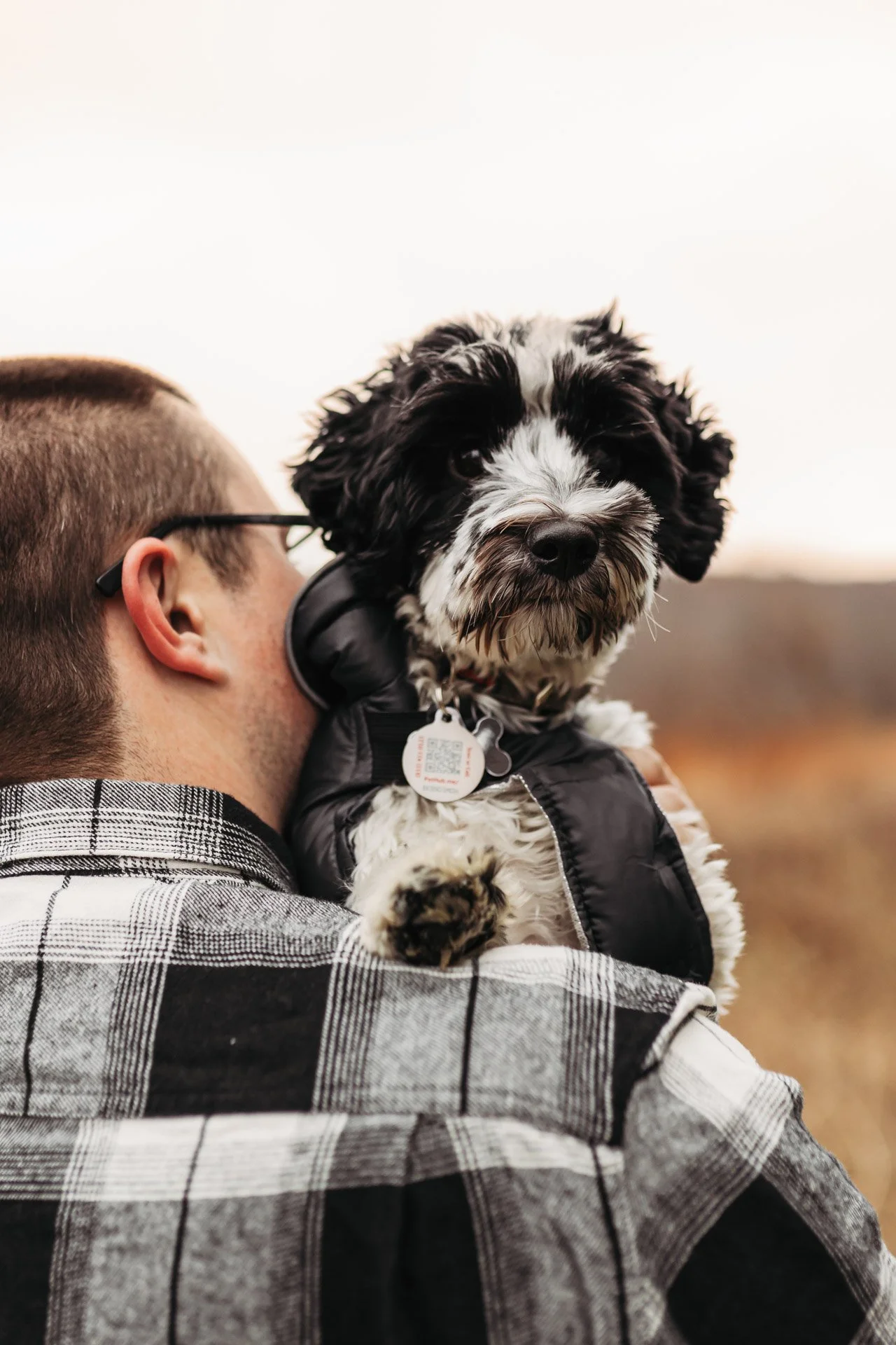 A man holding a black and white puppy in an outdoor setting during daytime