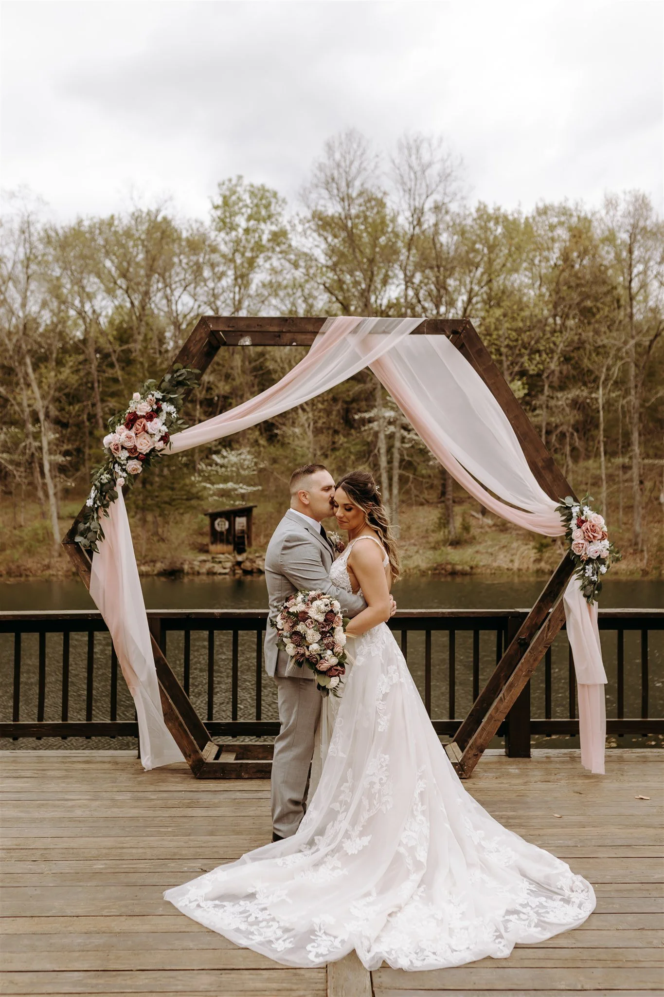 A bride and groom sharing a kiss under a wooden hexagonal wedding arch at Rolla, MO rustic wedding venue, The Village. Photos by Columbia, MO Photographer Liv Strange Photography.
