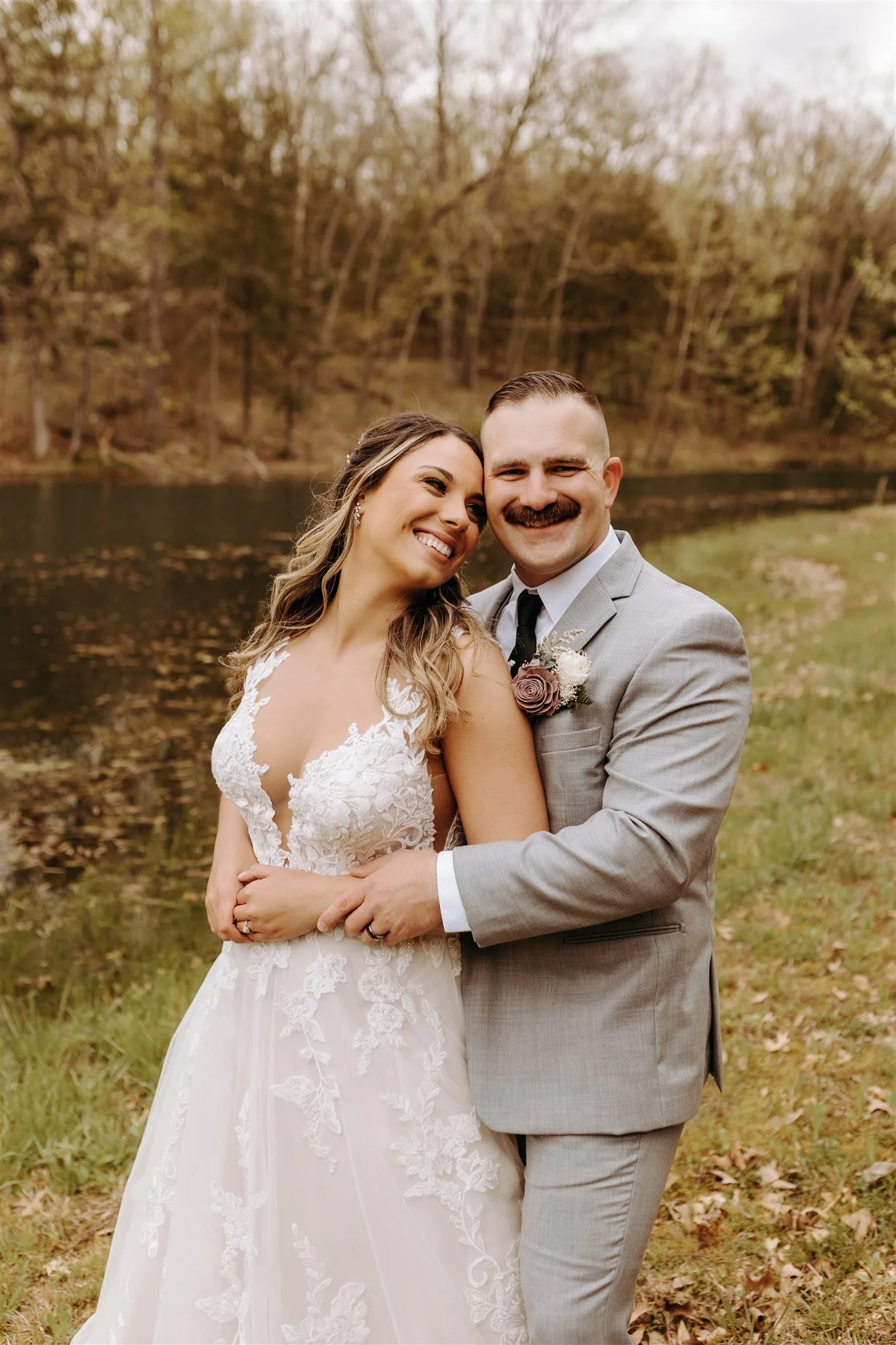 Happy bride and groom embracing outdoors near a lake with trees in the background at Rolla, MO rustic wedding venue, The Village. Photos by Columbia, MO Photographer Liv Strange Photography.