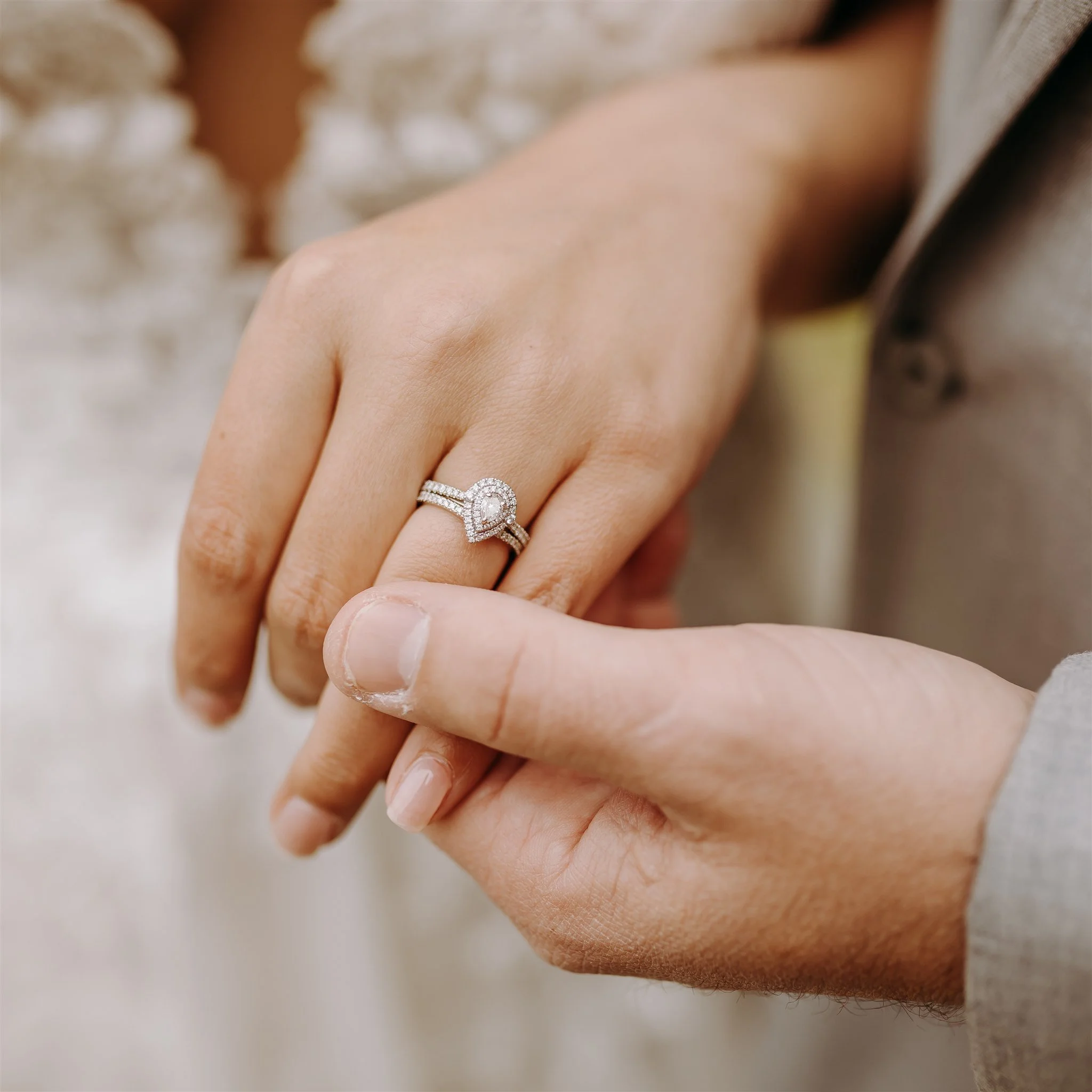 Close-up of a woman's hand with a wedding ring and engagement ring, showing the rings on her ring finger. A man's hand gently touches her finger at Rolla, MO rustic wedding venue, The Village.