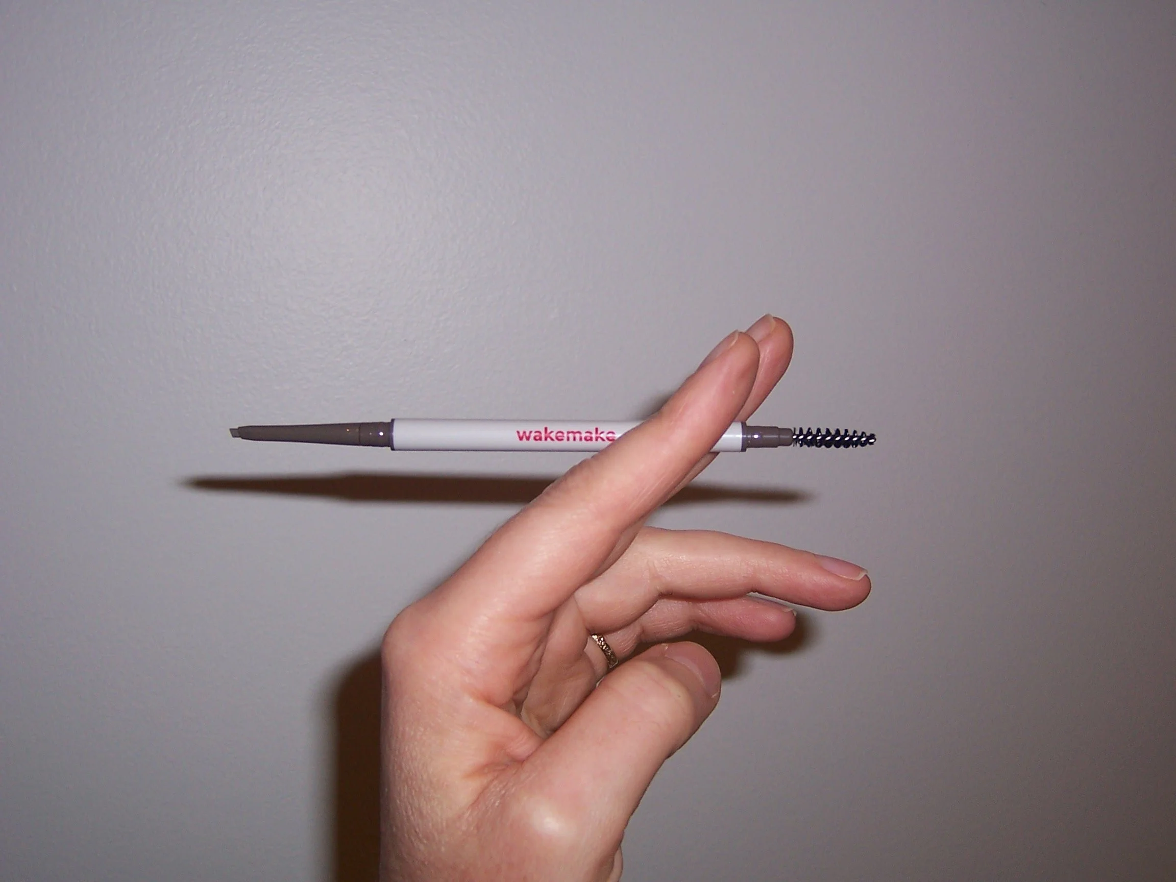 Hand holds Wakemake eyebrow pencil like a cigarette
