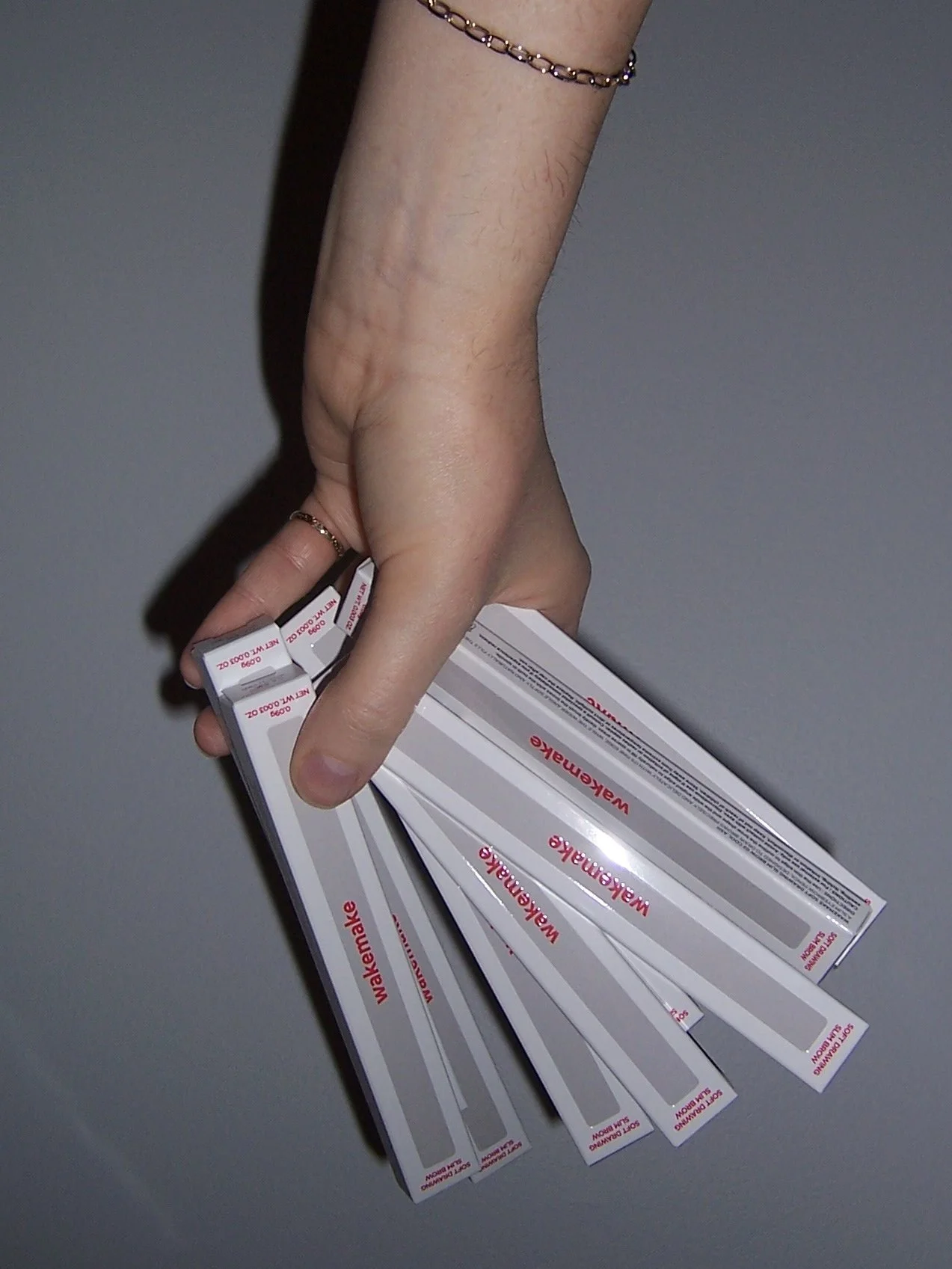 An upside down hand holds a fist full of Wakemake eyebrow pencils in their boxes