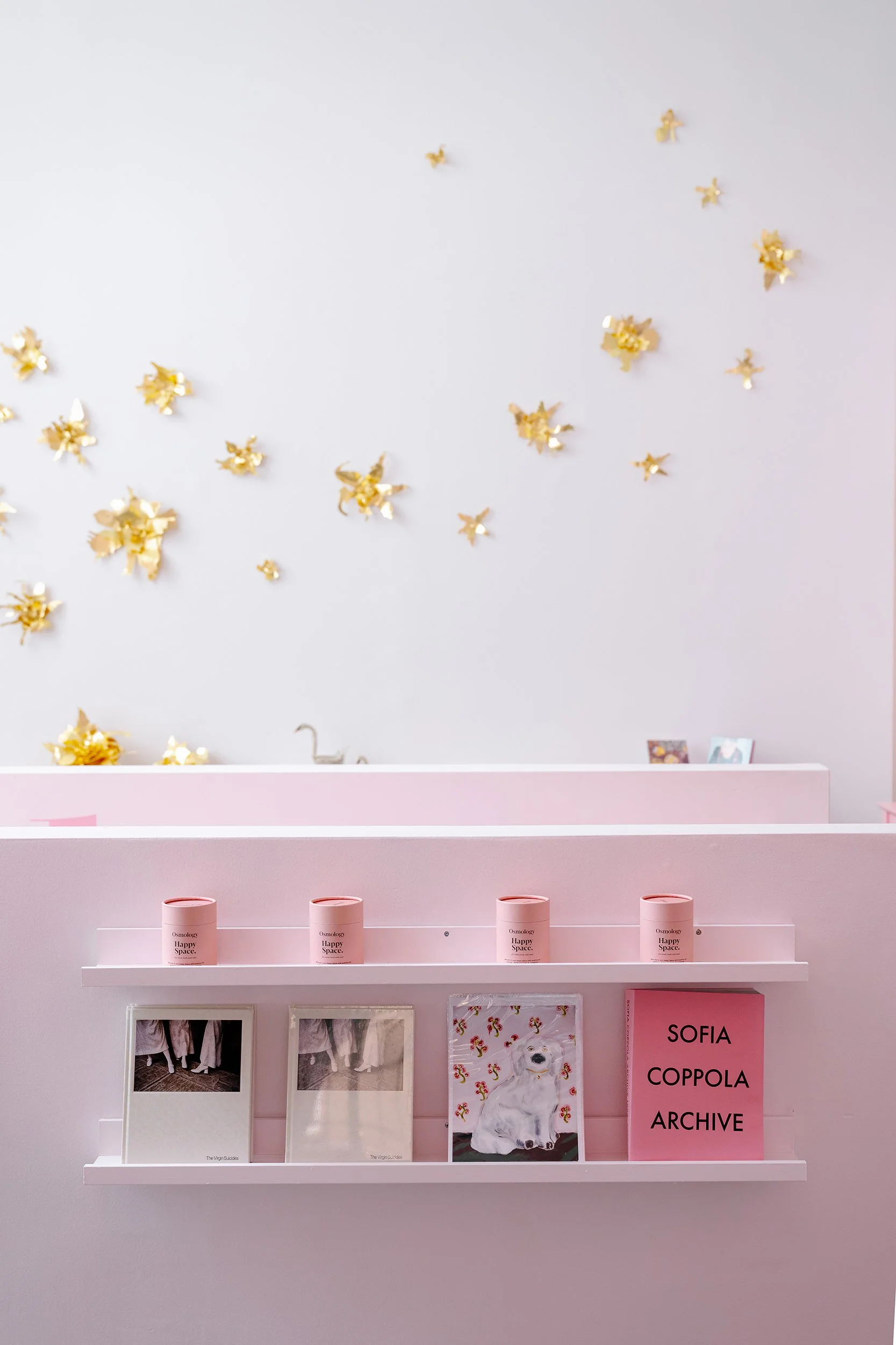A white wall decorated with multiple gold-colored metal flowers arranged in clusters.