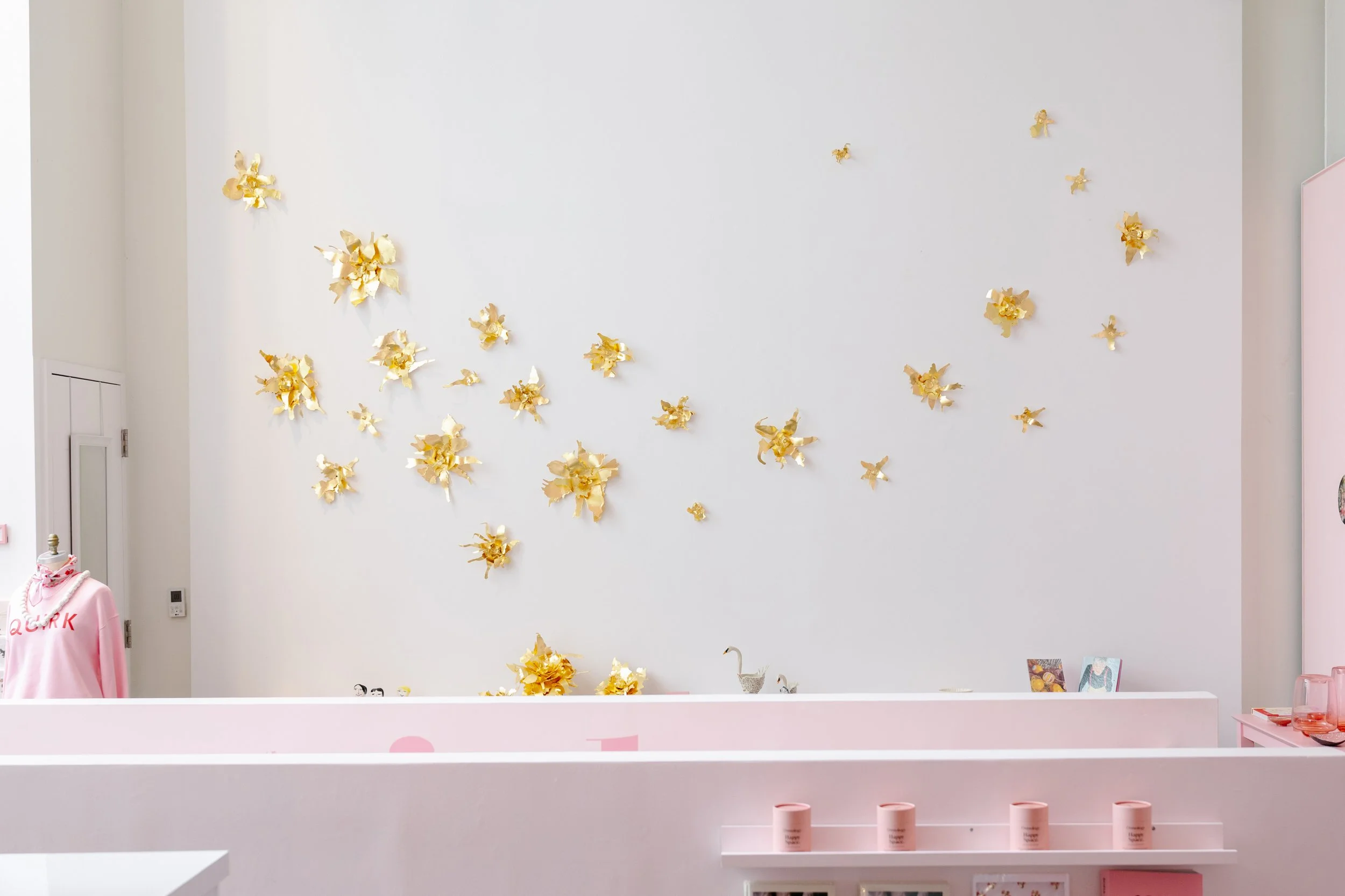 A white wall decorated with multiple gold-colored metal flowers arranged in clusters.