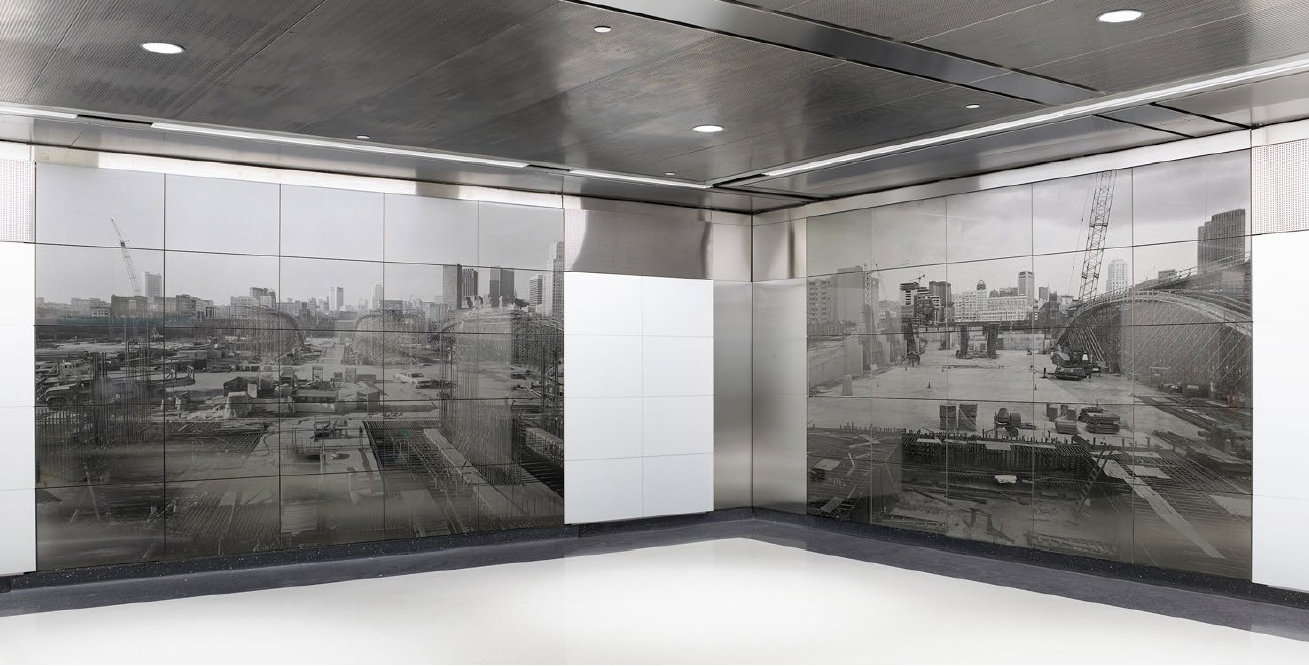 	
Black and white photographic mural depicting a construction site with scaffolding and buildings, located along a clean, modern hallway with reflective flooring and ceiling lighting.