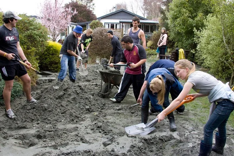 People working together to spread and level soil or gravel in a backyard garden during a landscaping or community service project.
