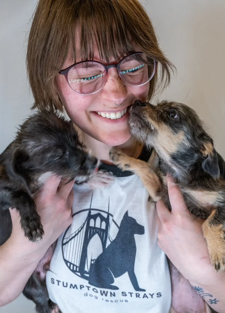 Stephanie smiles as two puppies kiss her face.