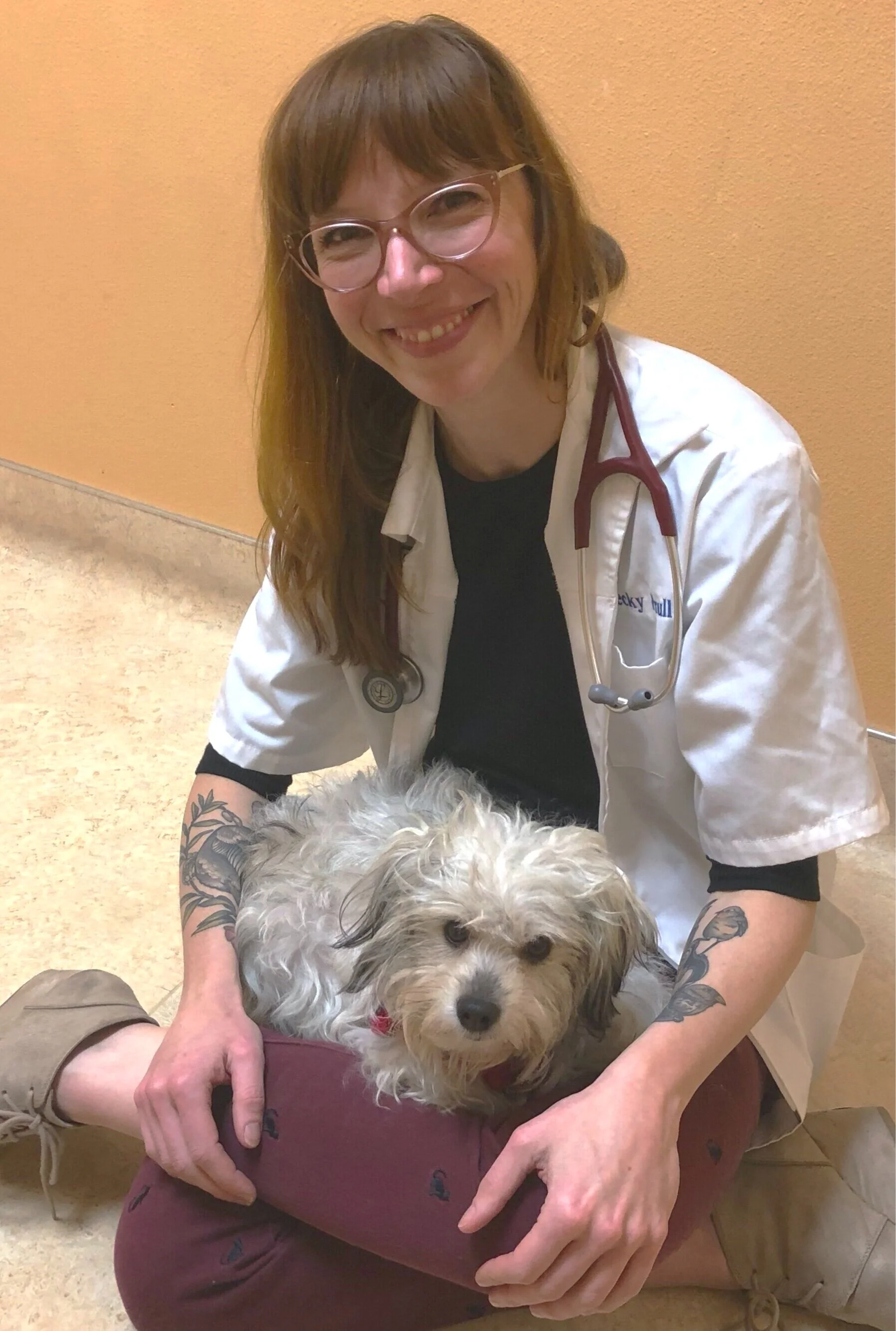 Beck sits on the floor with a gray and white dog in her lap.