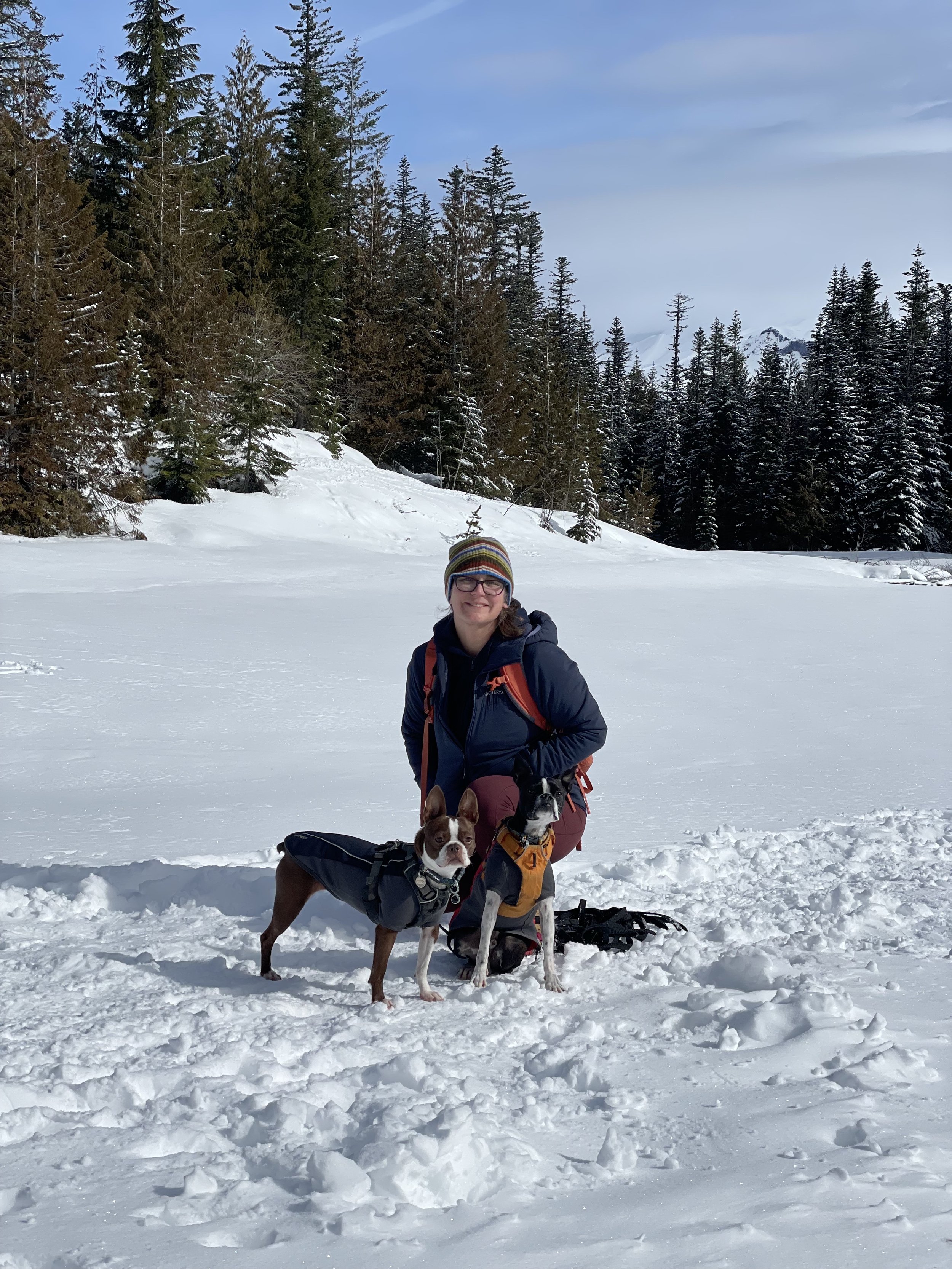Jennifer kneels on the snowy ground with her two dogs.