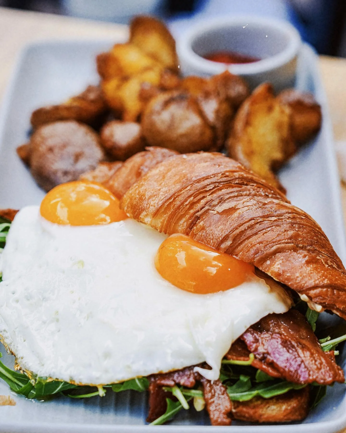 Assembled to perfection. 🤌🏼 Get the Croissant Breakfast Sandwich made with two sunny side up eggs, crispy bacon, arugula, roasted garlic aioli, toasted @breadandcie croissant.