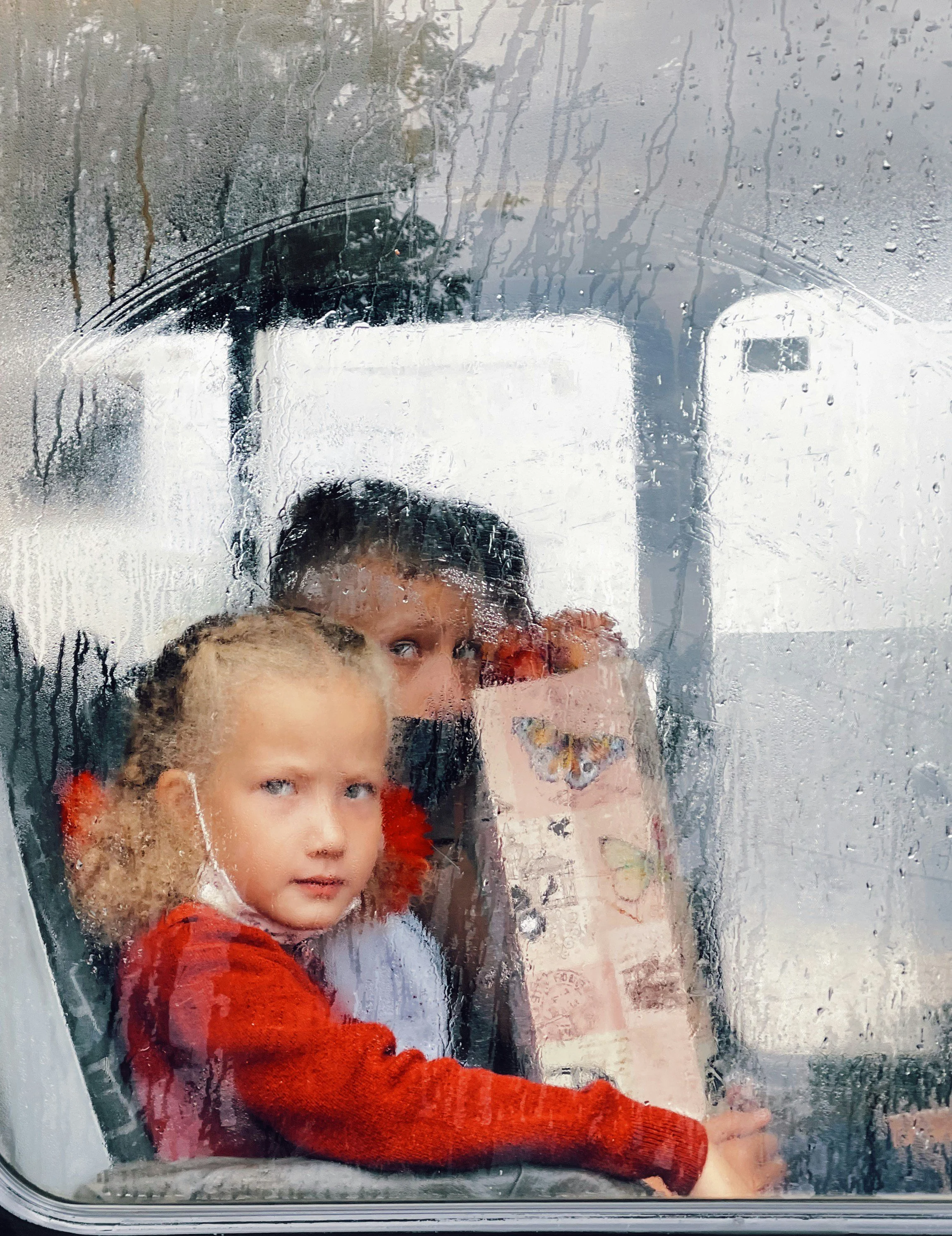 Photo of two children looking out the window of a bus on a rainy day.