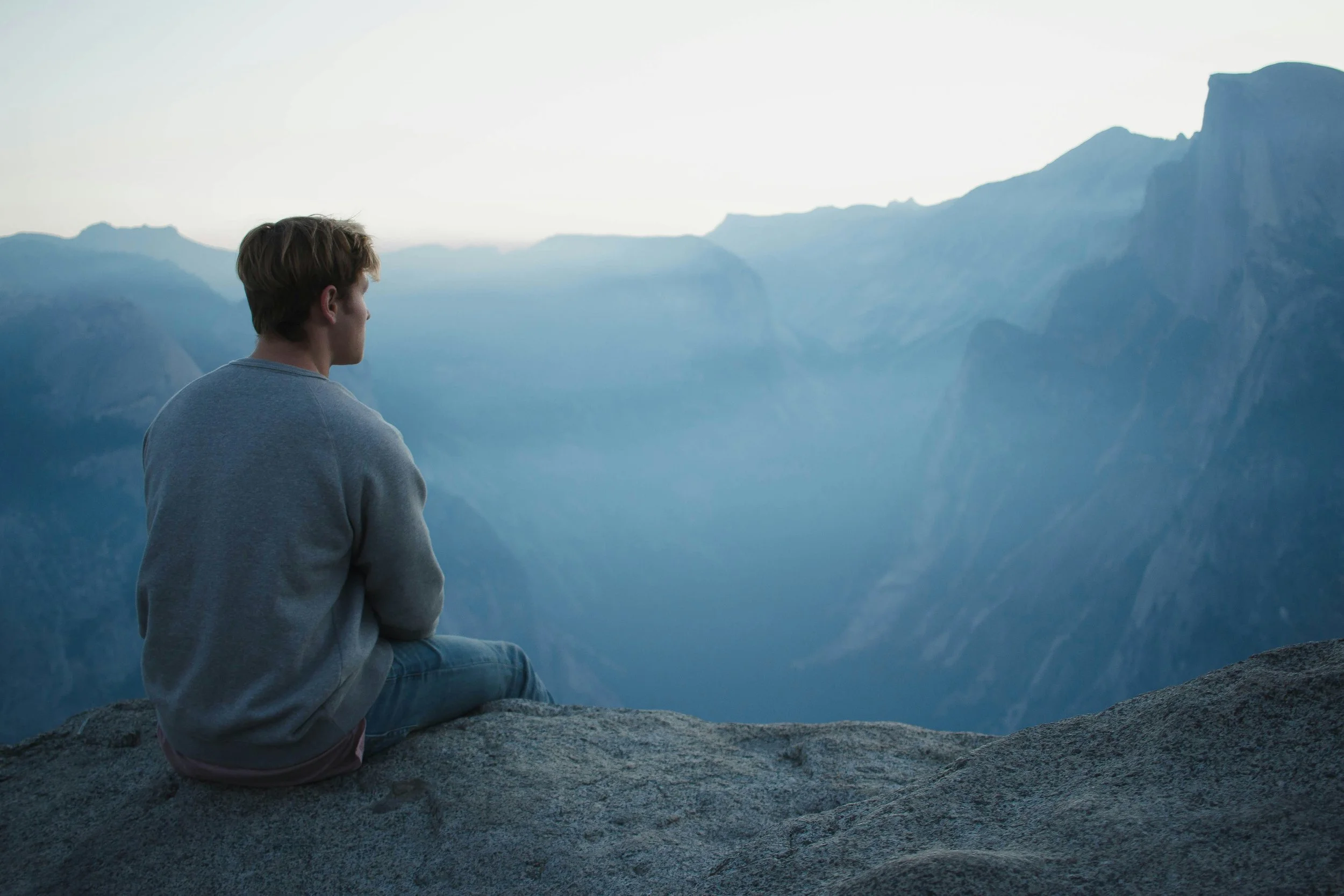 Image of a younger man sitting on a rock looking at the horizon.