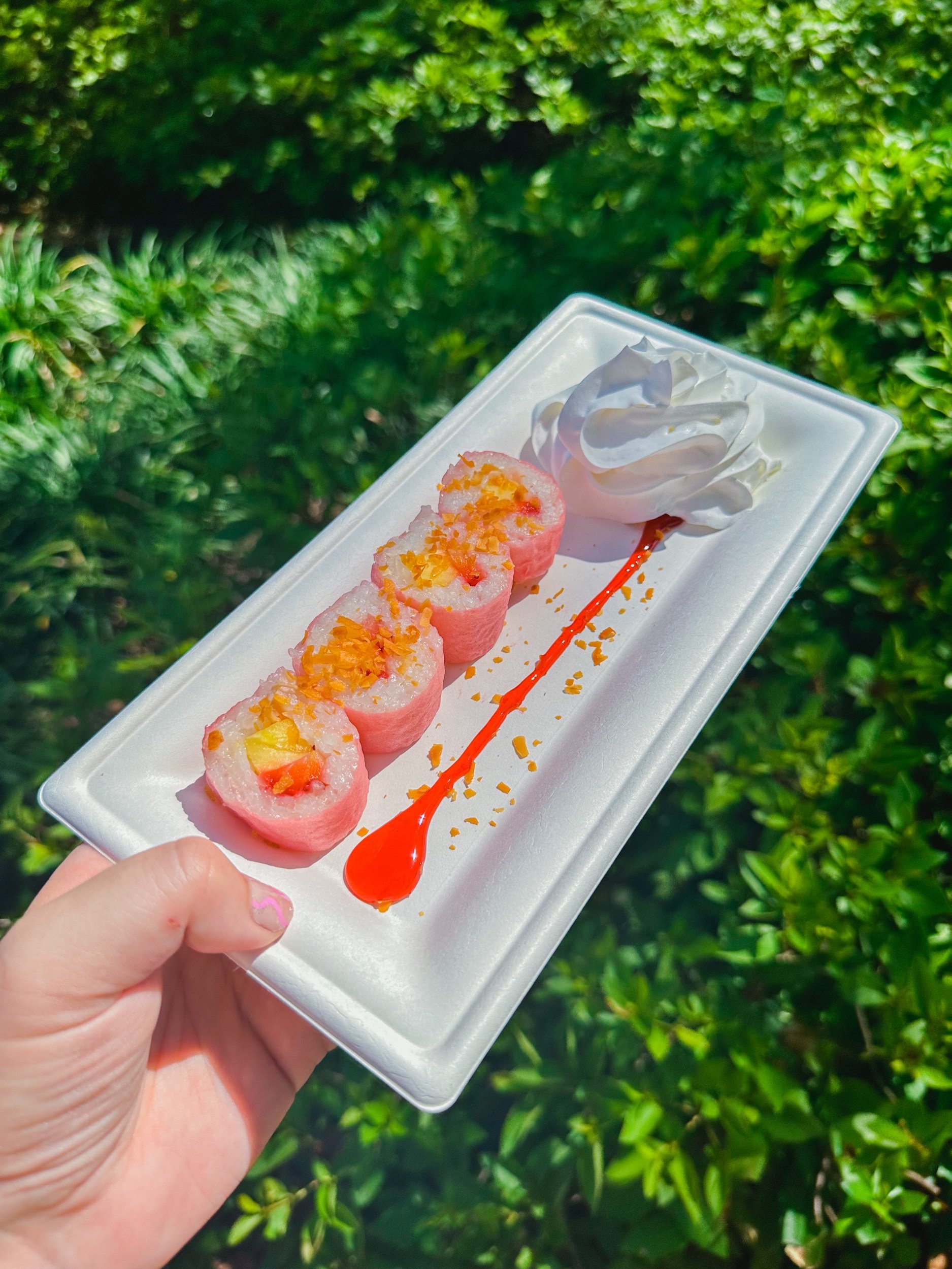 Frushi: Strawberry, pineapple, and lychee wrapped in coconut rice and pink soy wrap served with whipped cream, drizzled raspberry sauce, and toasted coconut