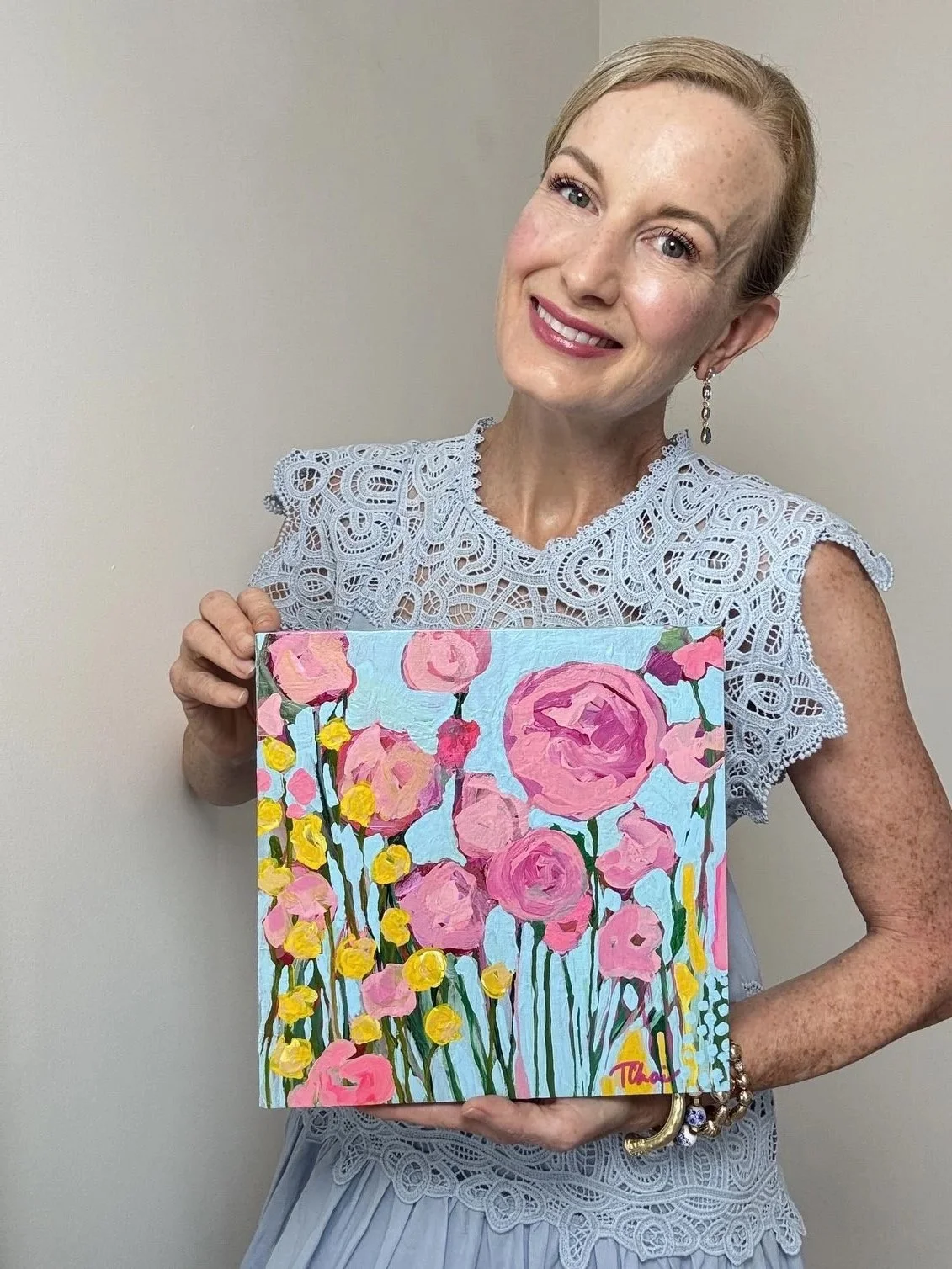 a smiling woman is holding a painting of yellow and pink flowers on a blue background