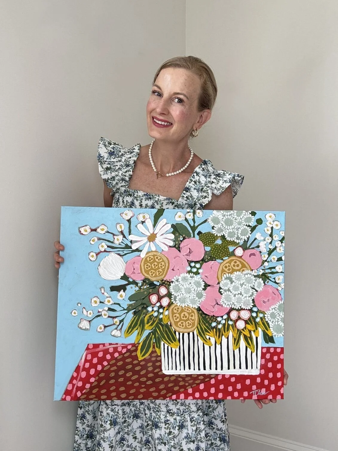 a woman is smiling holding a painting of a bouquet of pink, yellow and white flowers