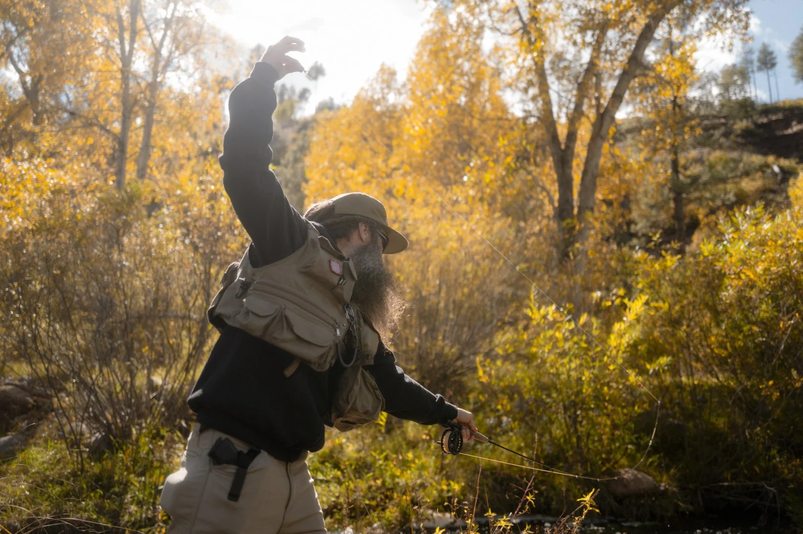 Man fly fishing in a river surrounded by fall foliage with orange and yellow leaves.