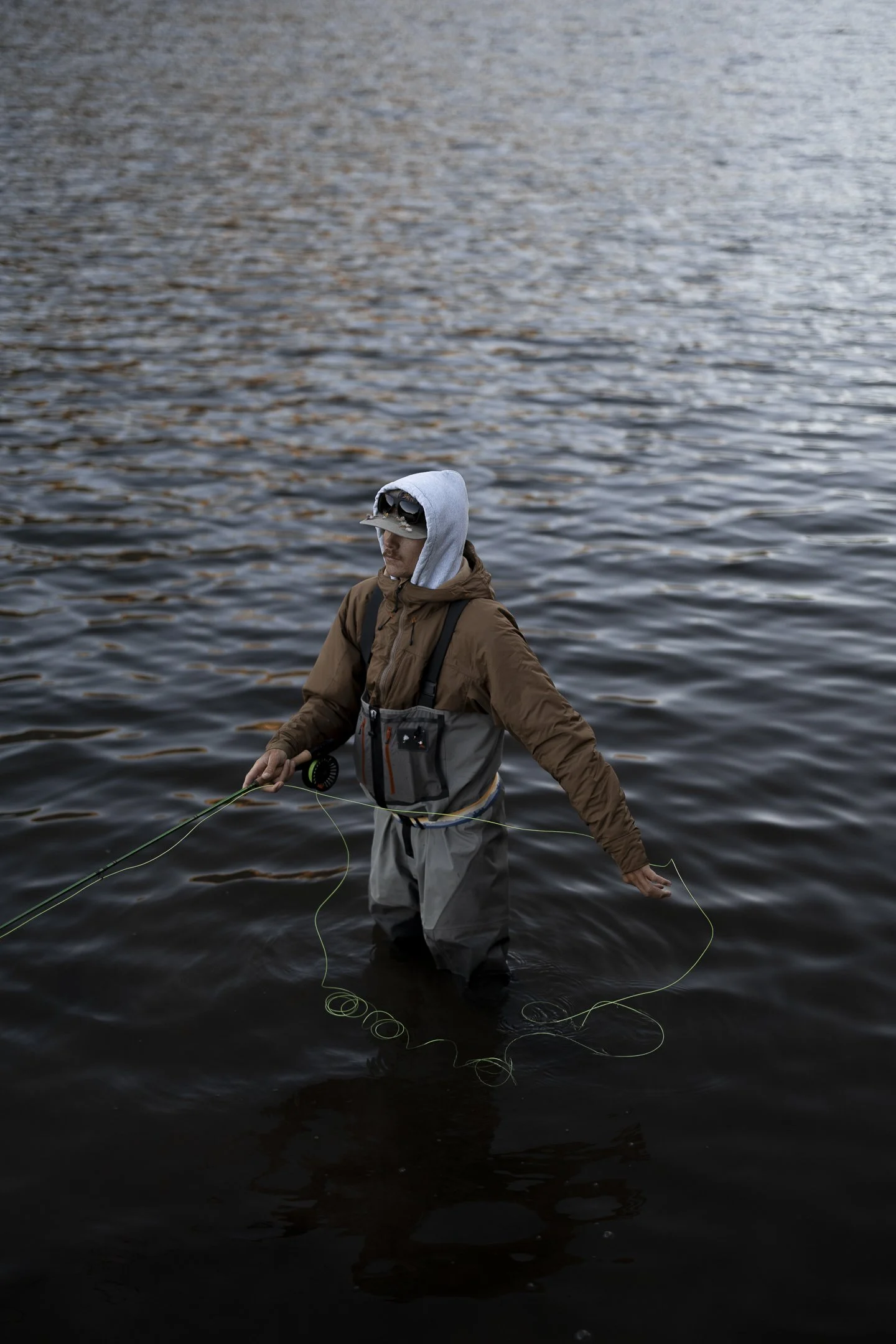 Person wearing waterproof gear, standing in water and fly fishing with a fishing rod.