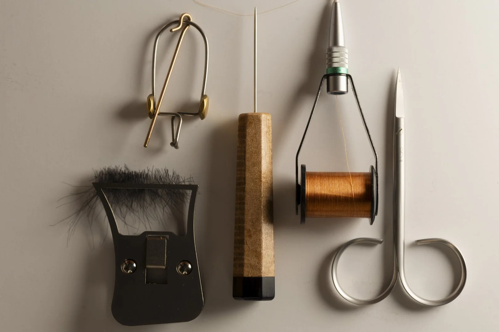 A collection of shaving and grooming tools including a shaver blade, a file, a needle, a spool of thread with a needle, a pair of scissors, and a utility knife arranged on a flat surface.