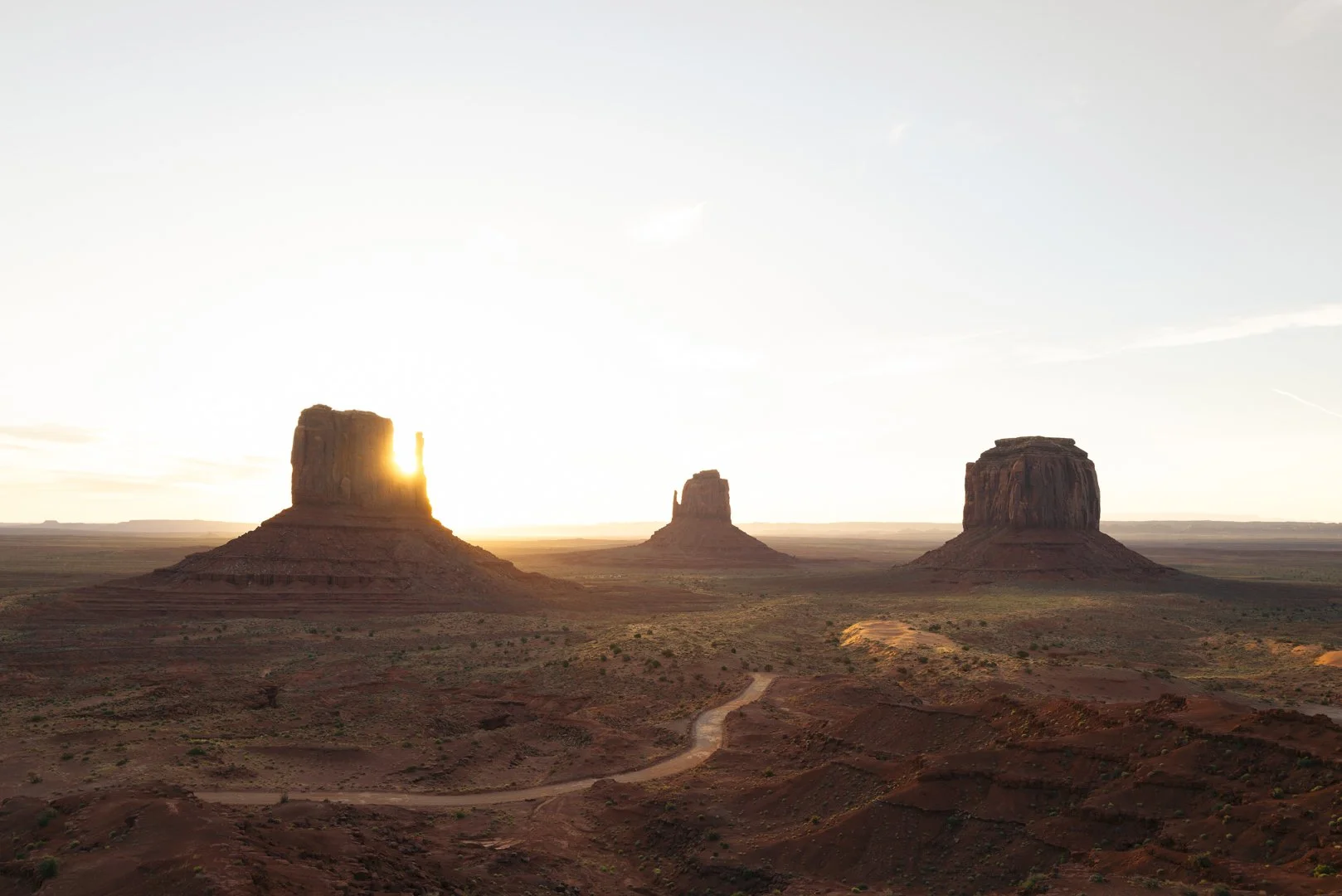 Sunset over Monument Valley with three large sandstone buttes in the desert landscape.