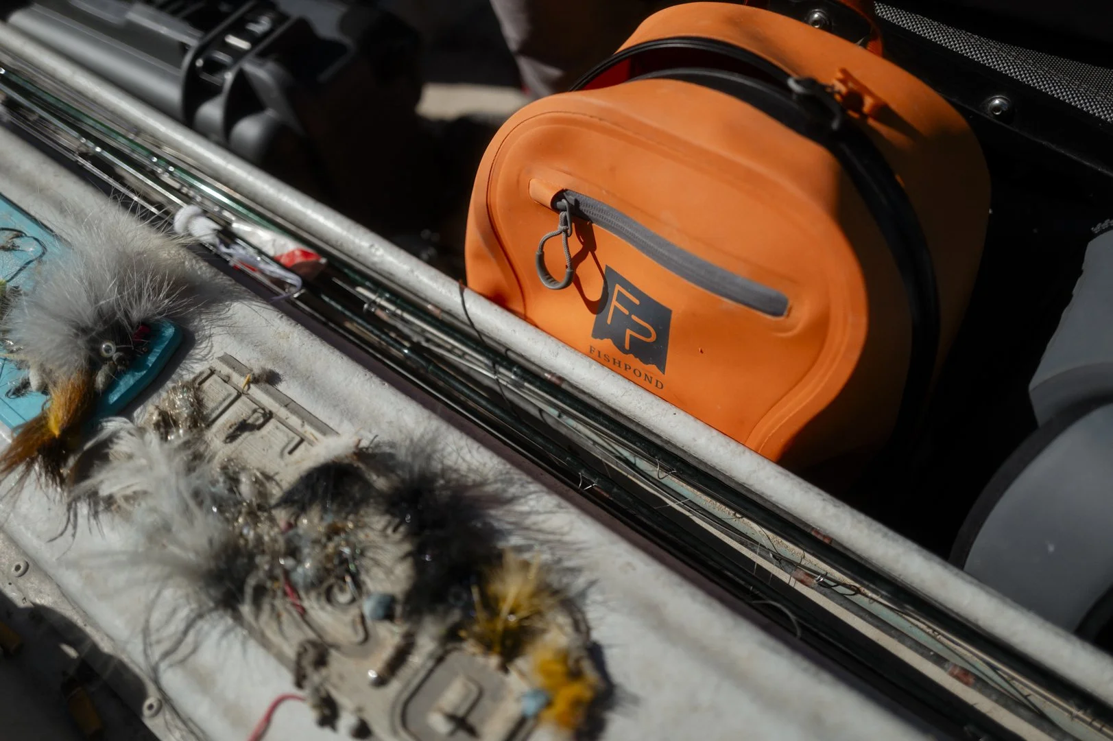 Close-up of fishing gear including orange waterproof box, tackle modifications, and fishing flies.