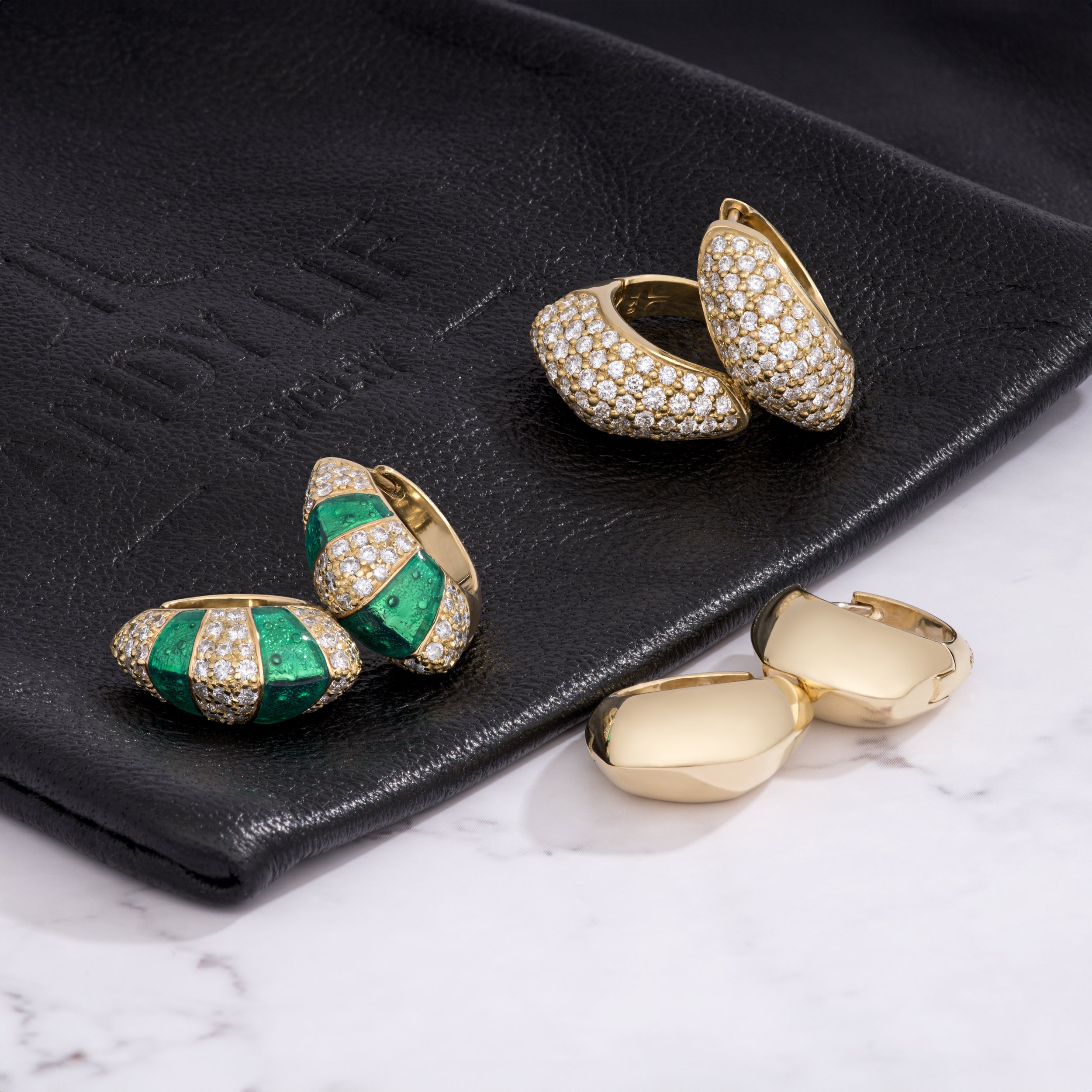 Gold and diamond studded earrings with green accents placed on a black textured jewelry box.