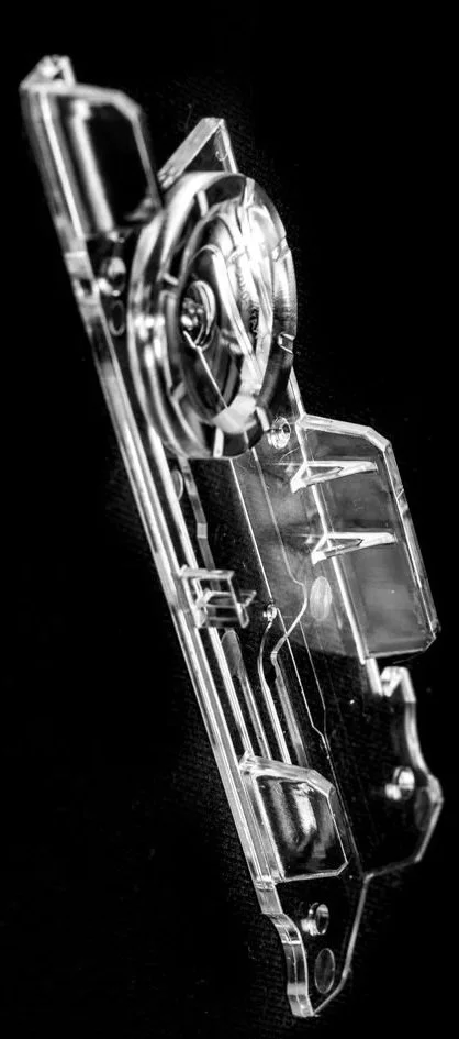 Close-up of a transparent microfluidic injection moulded IVD device on a black background.