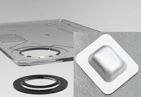 Close-up of a silver-coloured reagent blister pouch containing IVD reagents and a credit card sized, transparent injection moulded part with integrated pump (PumpRing)