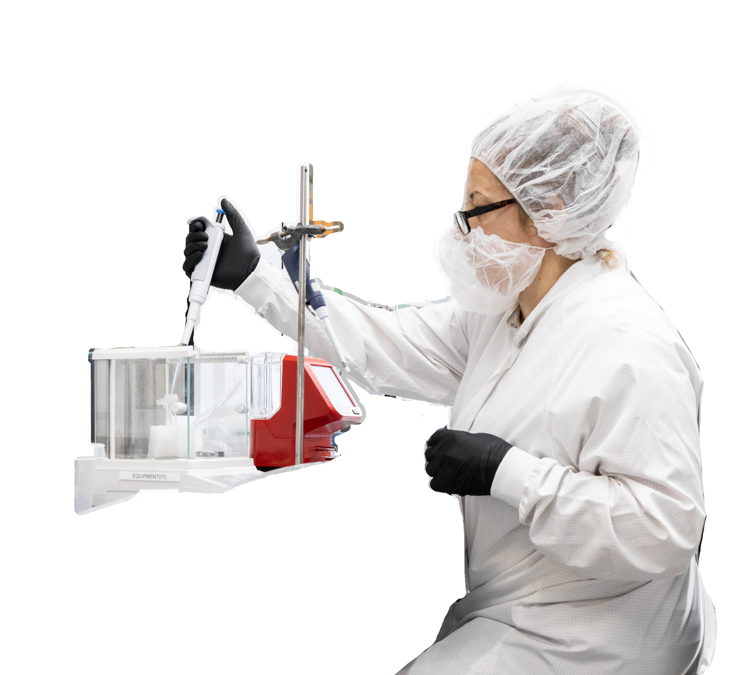 A scientist wearing a white lab coat, black gloves, hairnet, and face mask is working with laboratory equipment, pipetting a liquid into a container.