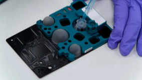 QuantuMDx Q-POC PCR test cartridge held by a lab technician wearing purple gloves