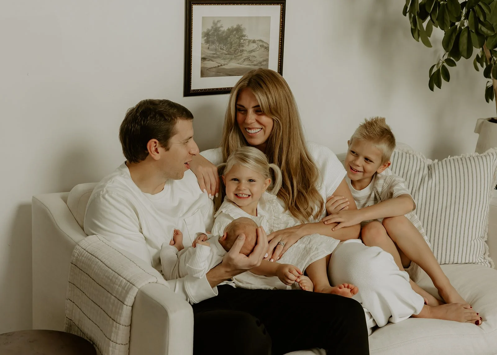 A family of five in their home sitting on a white couch and smiling at each other.