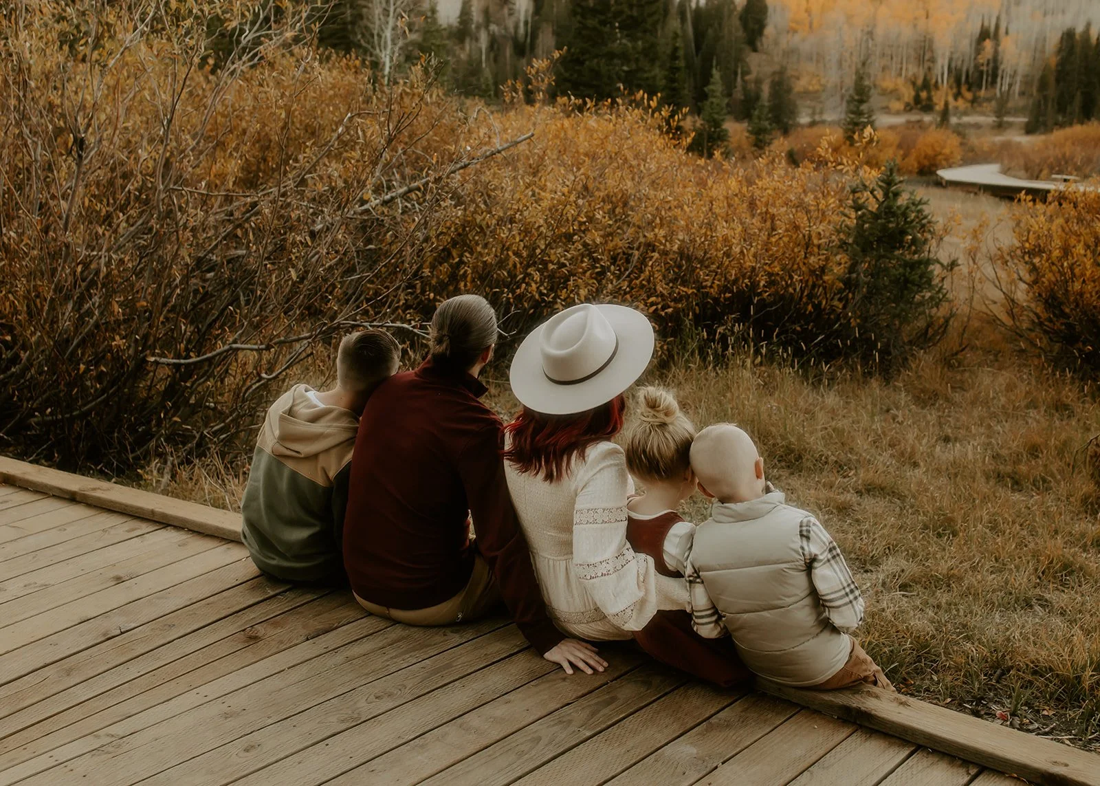 A family of five sitting outside admiring the fall leaves in the Utah mountains.