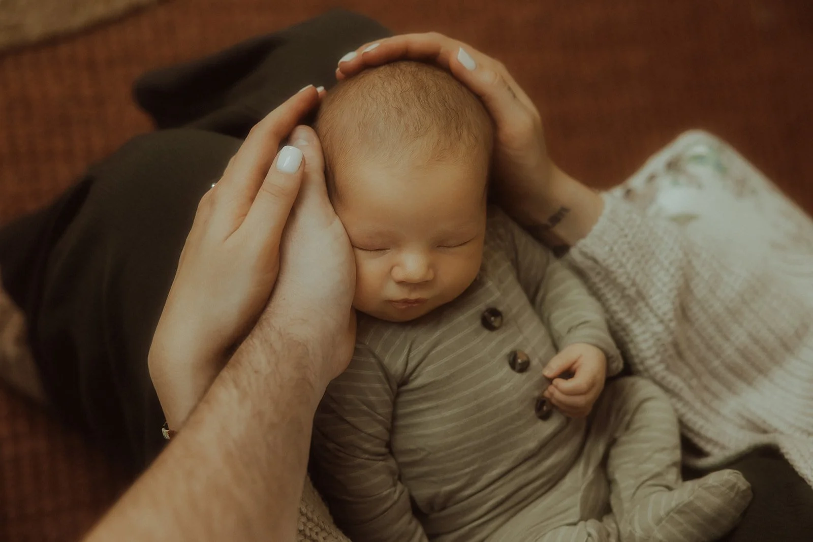 Two parents cradling their newborn baby's head.