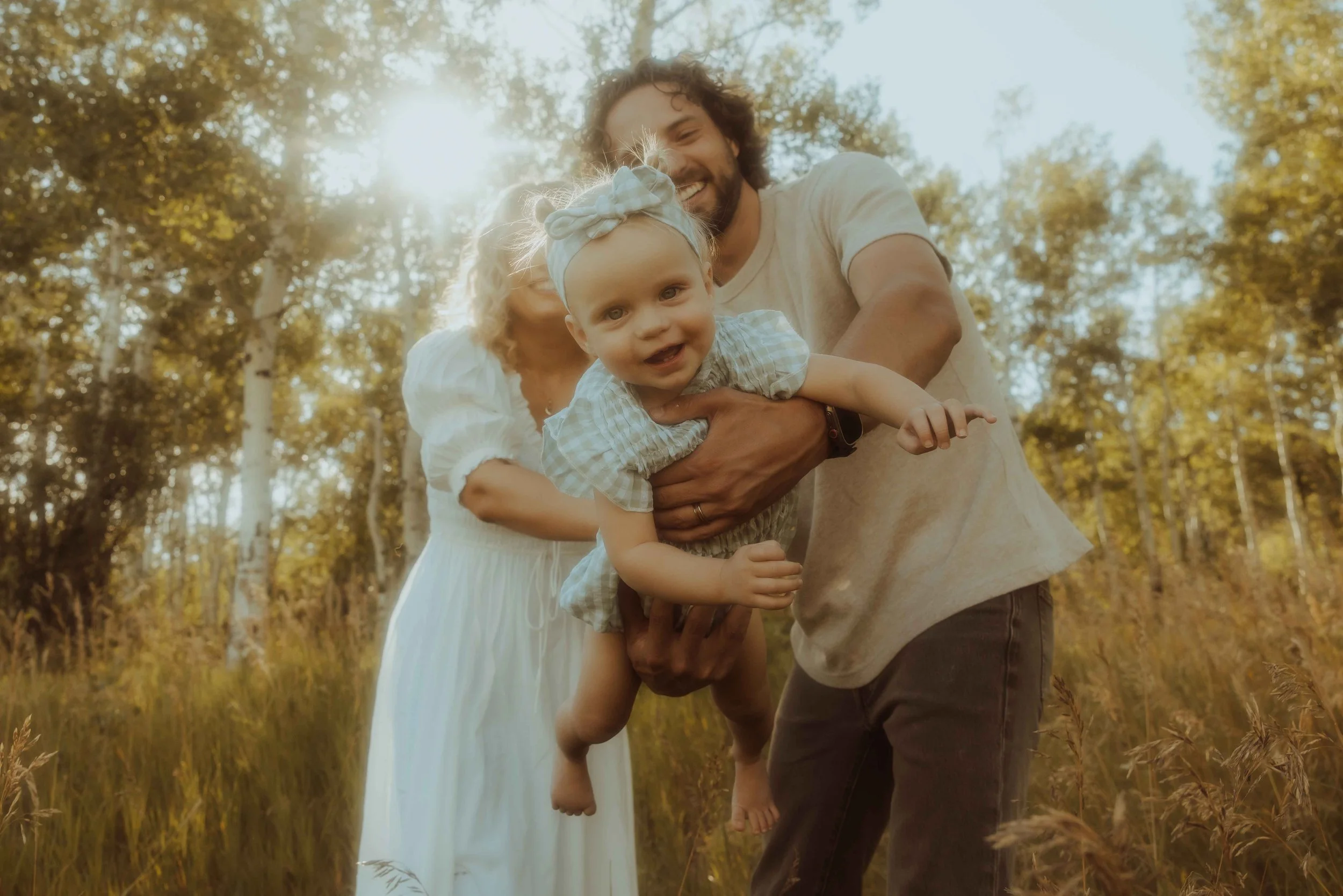 A baby girl being swung in the air by her parents while outside in the mountains on a summer day.
