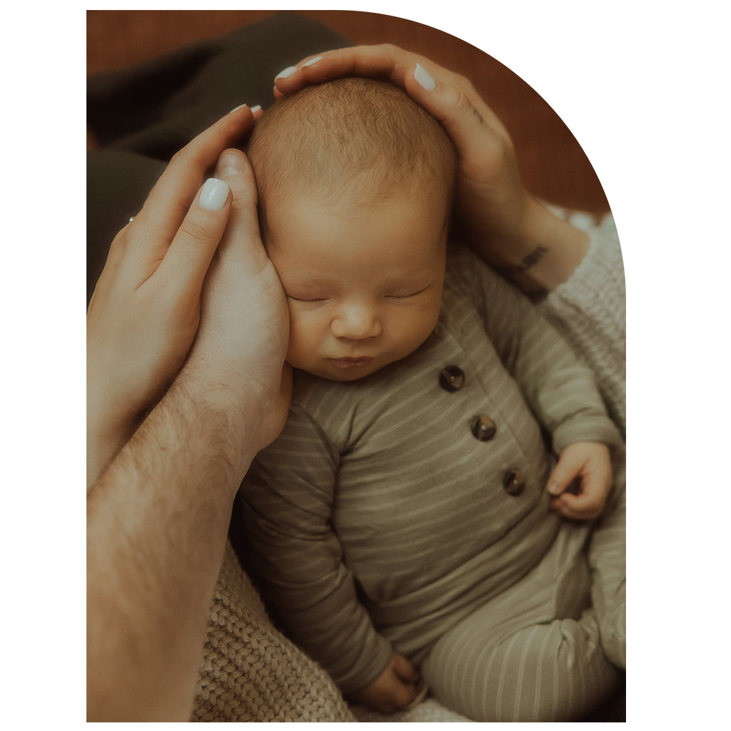 A newborn baby boy laying in his mother's lap while hands are cradling his head.