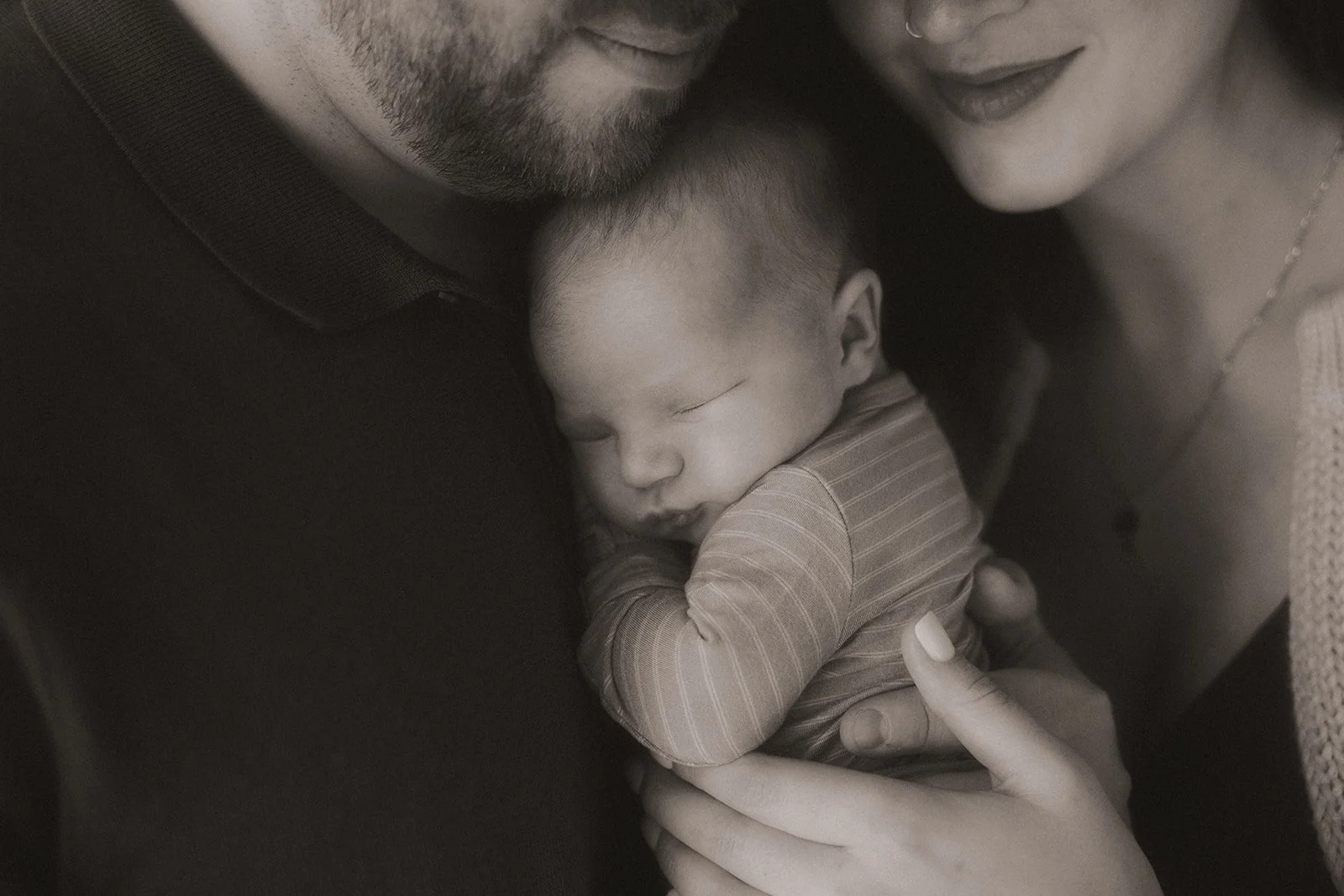 A family of three snuggling their newborn baby in a cozy in-home Utah newborn photo session.