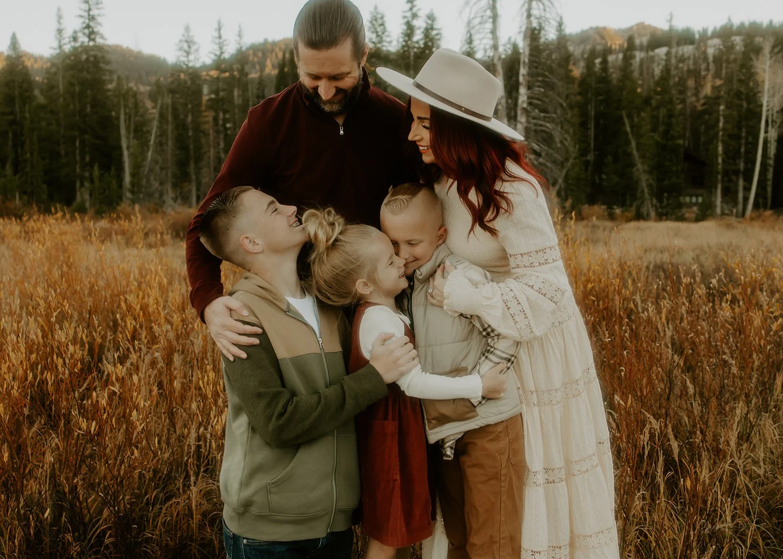 A family of five snuggling close together while standing outside surrounded by fall leaves.