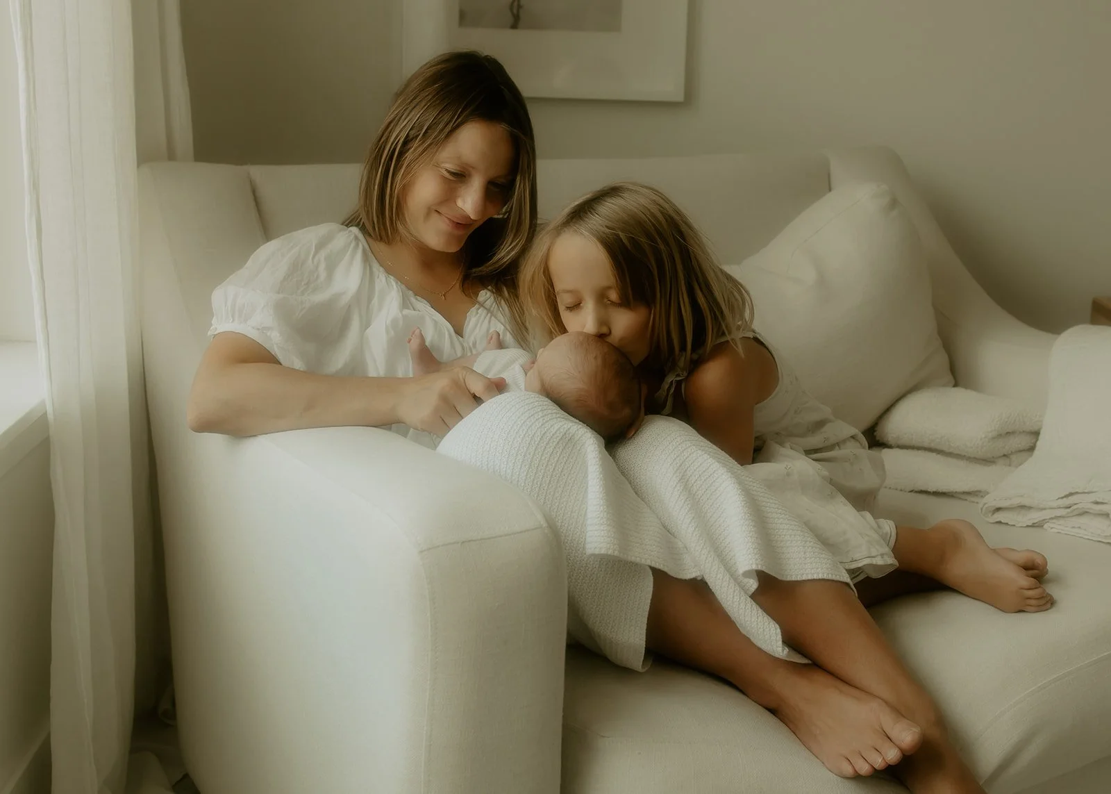 A mother and her children sitting on a white chaise smiling and embracing each other.