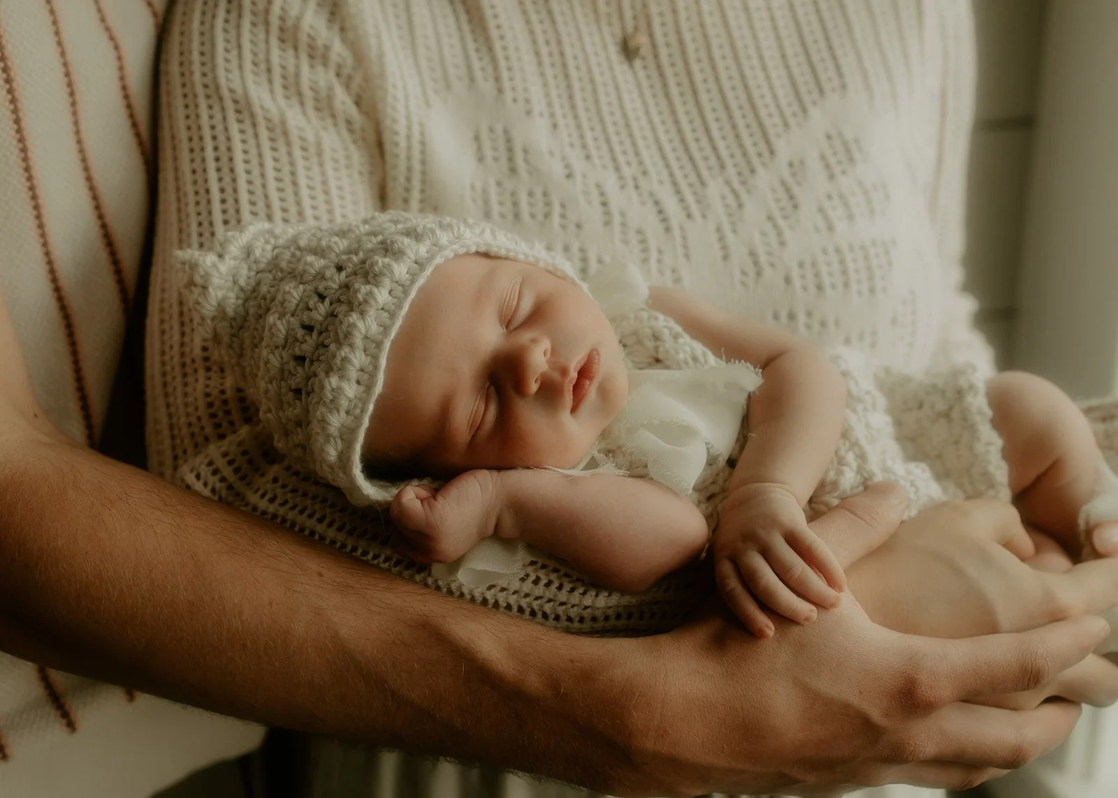 A newborn baby girl asleep and lying in her parent's arms.