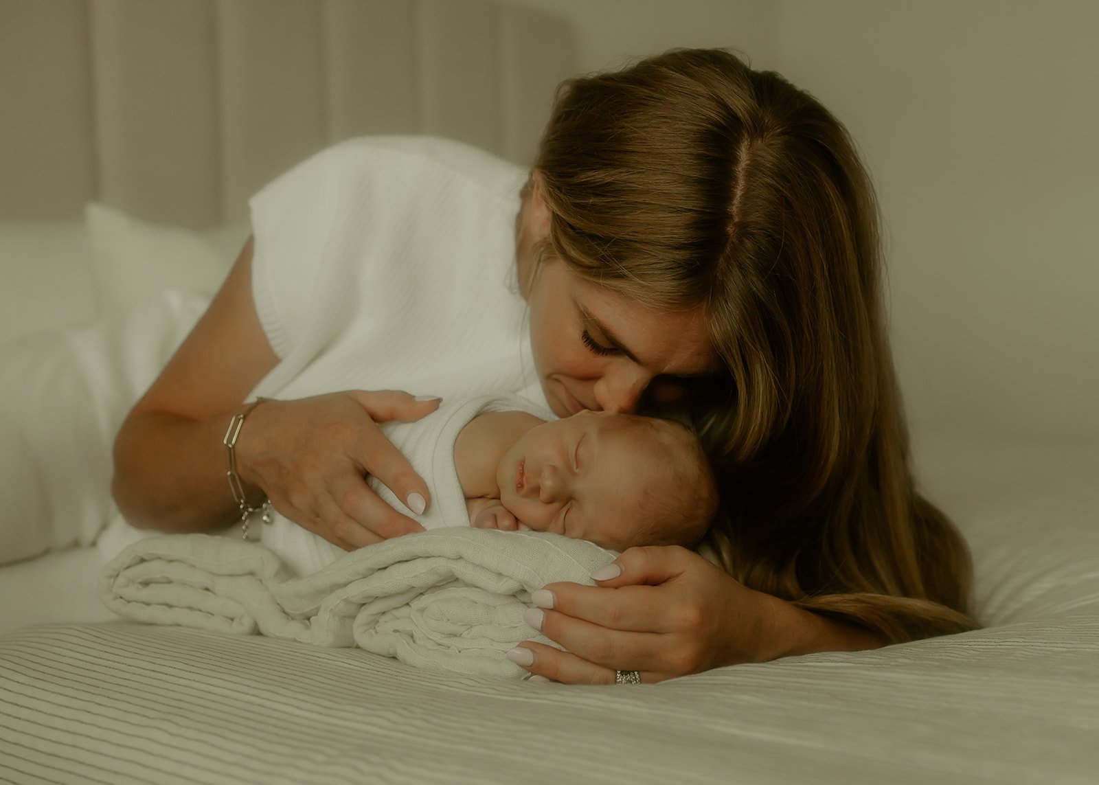 A mother laying on a bed and snuggling her newborn baby.
