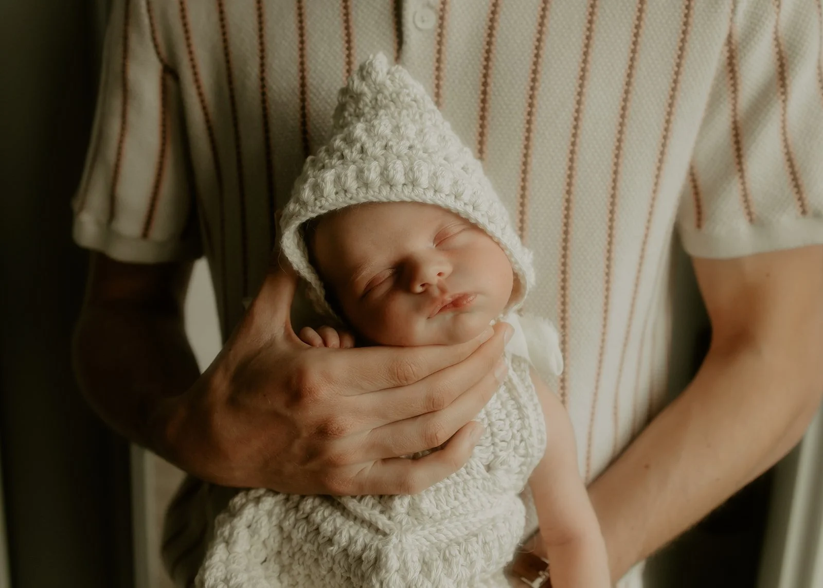 A newborn baby girl being held upright by her dad.