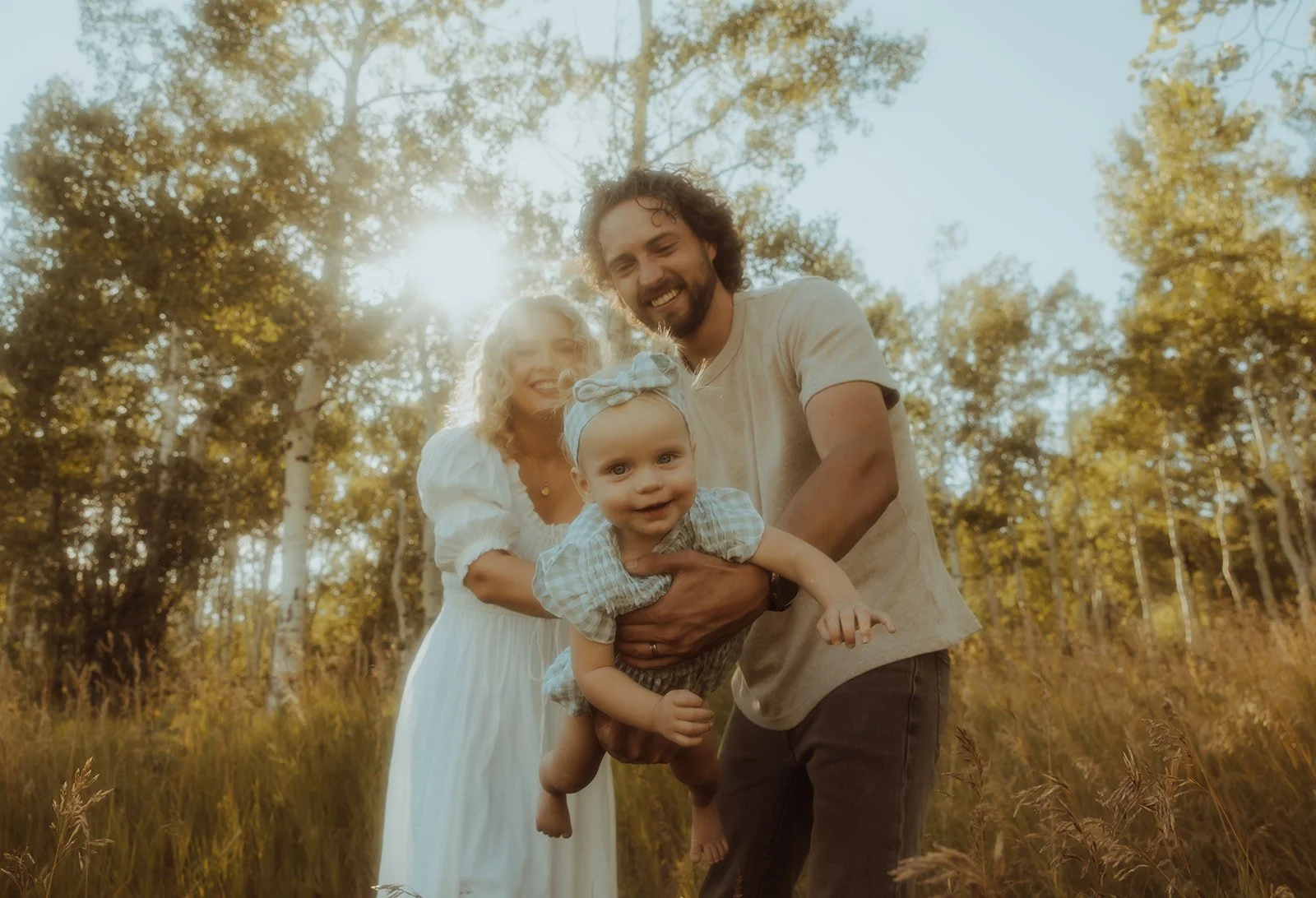 A husband and wife playing with their baby daughter in a meadow during the summer season.
