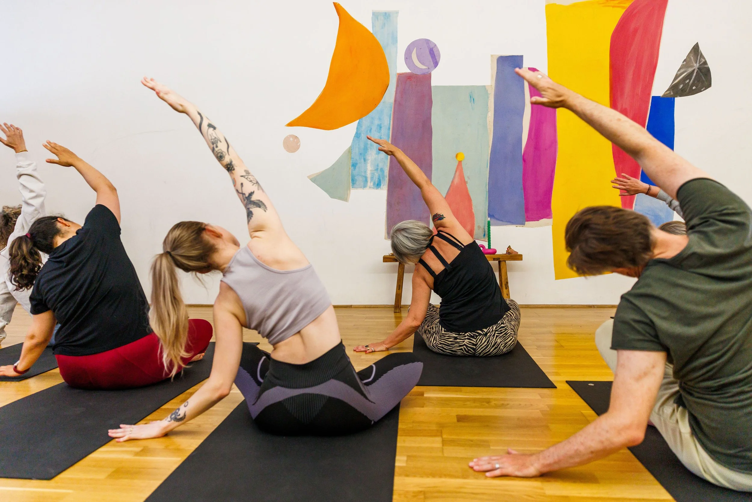 Clinty Thuijls van Adem en Eva ademcoach en yogadocent Amsterdamin  yogahouding op yogamat, lachend, in een yogastudio met yogamatten die ontspannend zitten.