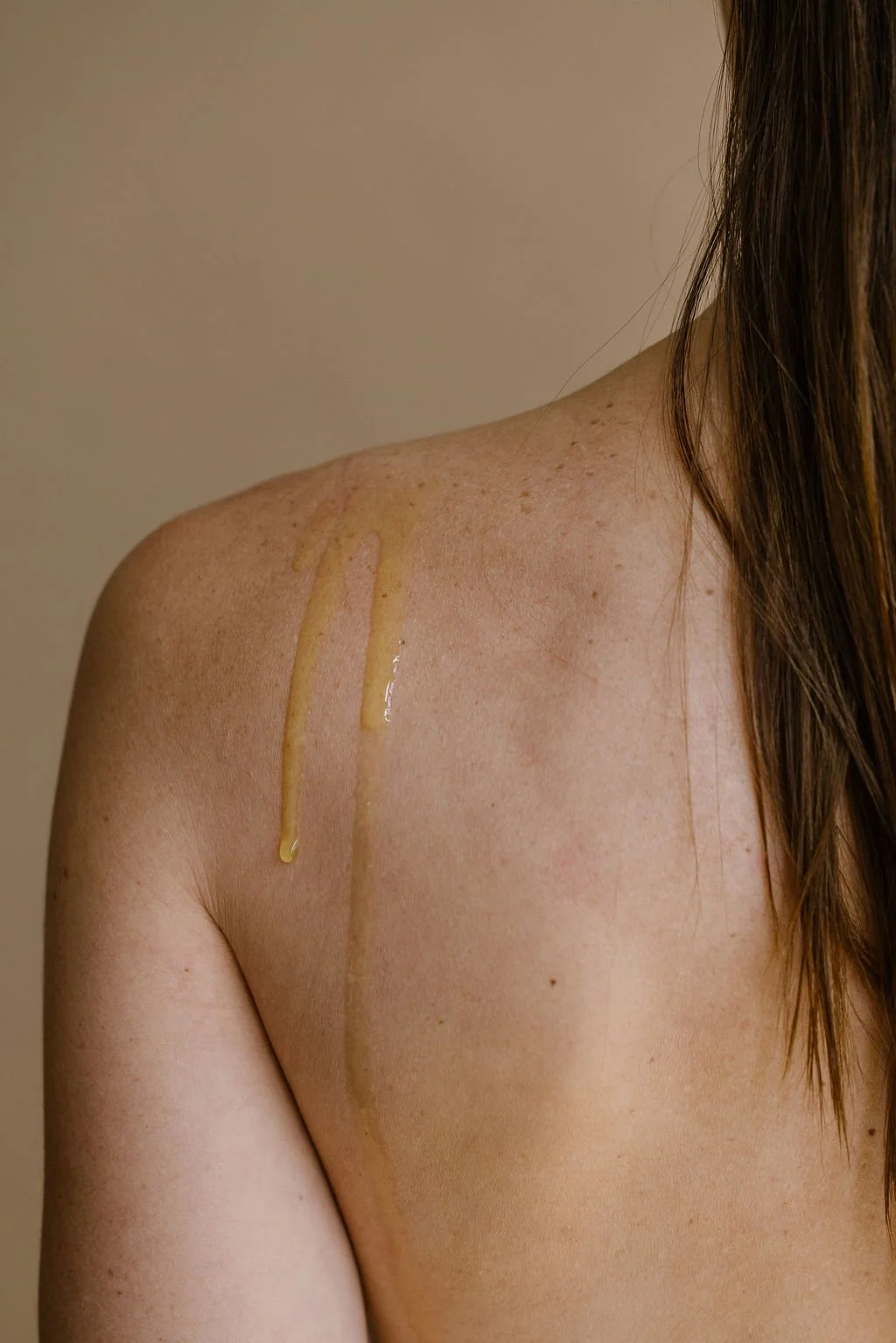 Une photo d'une épaule d'une femme avec de la crème ou de l'huile appliquée dessus.