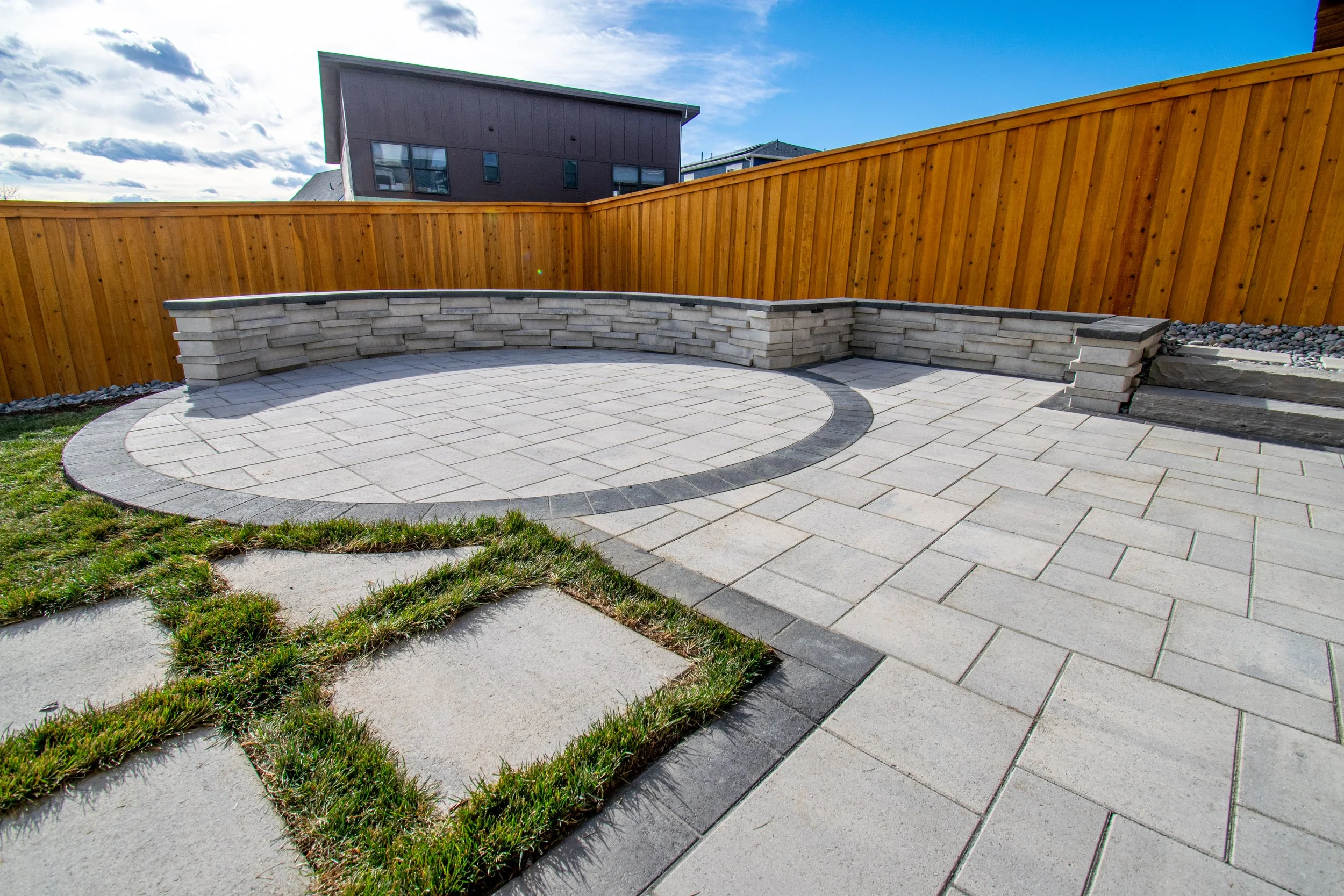 A modern backyard paver patio in Superior, CO with seated bench, stone steps, sod, mulch, grass and landscape lighting.