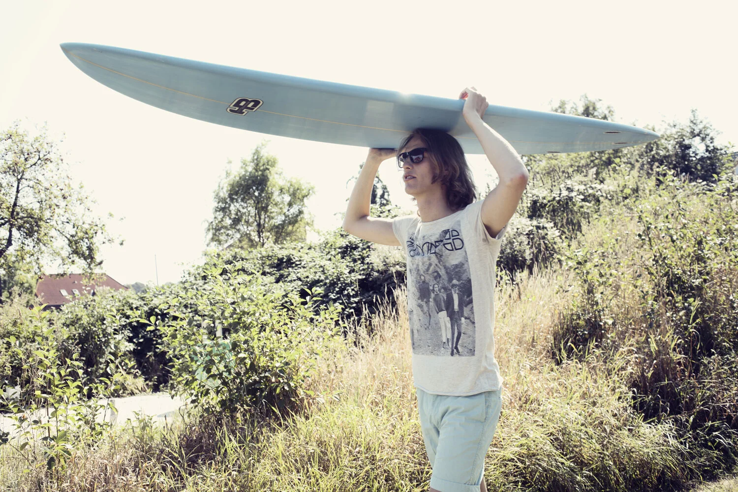 Ein junger hipster trägt ein Surfboard auf seinem Kopf