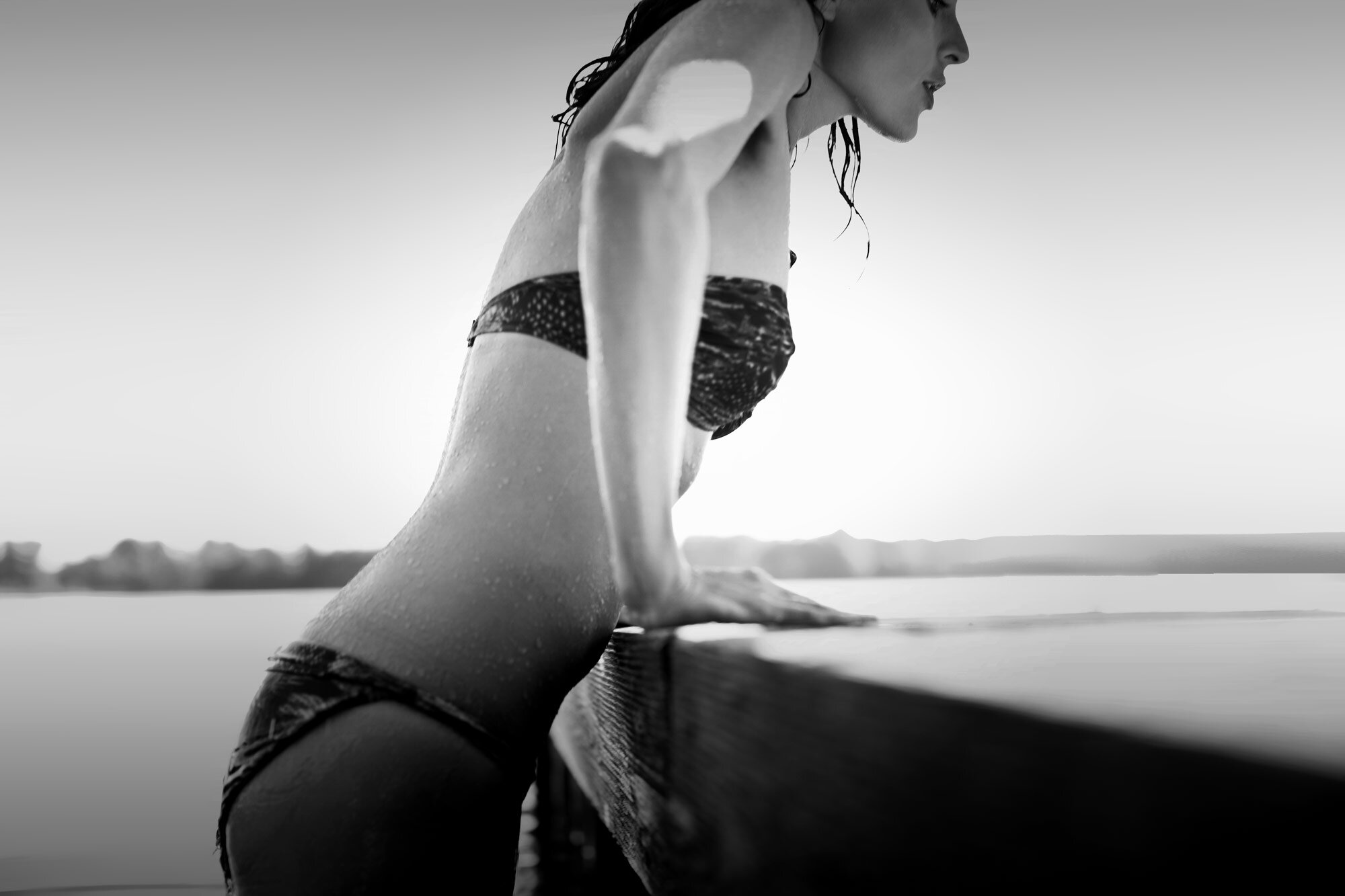 Eine junge Frau im Bikini drückt sich mit den Händen an einem Steg aus dem Wasser hoch